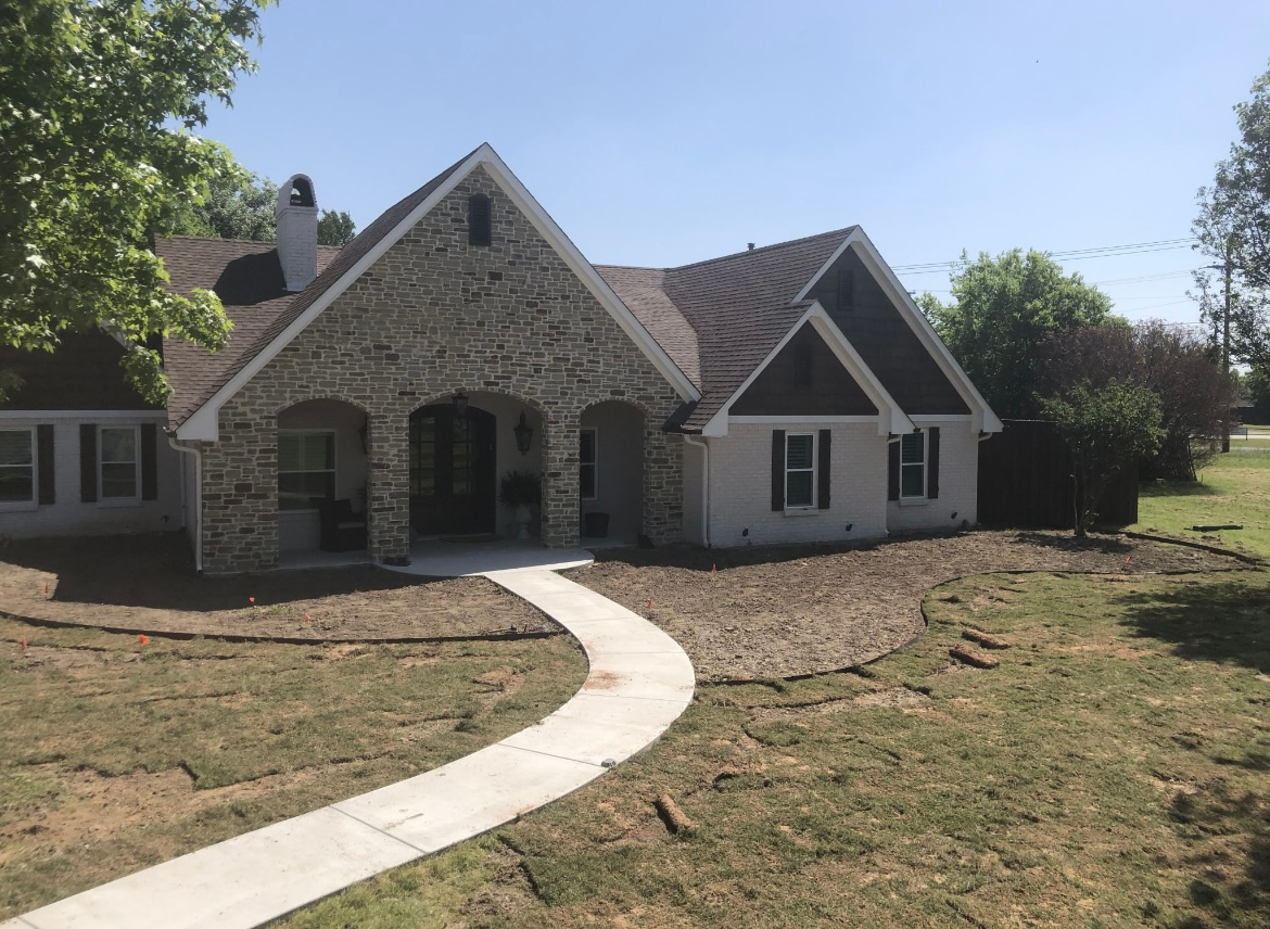 Stone house with arched front porch and curved walkway in a sunny yard
