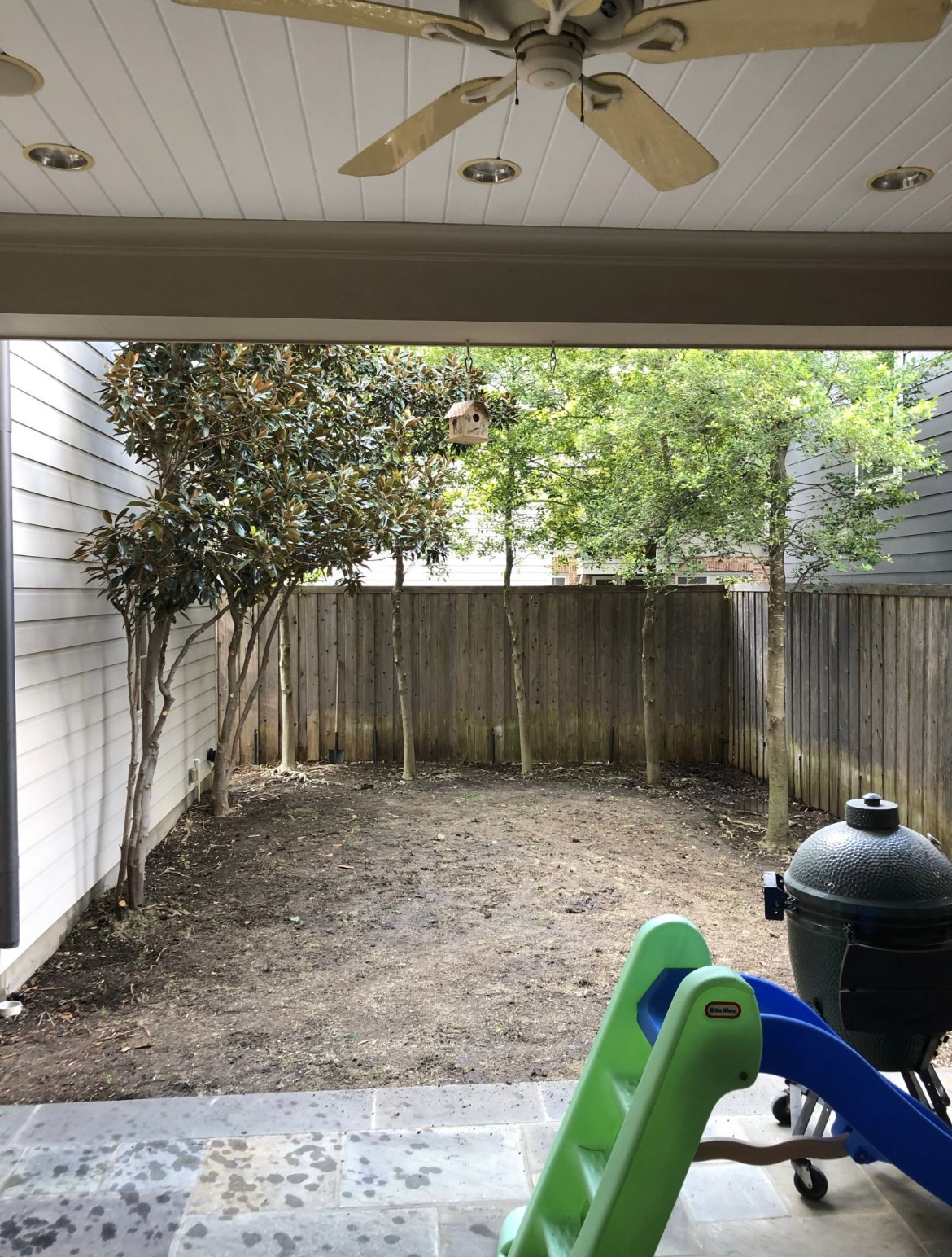 Covered patio facing a small fenced backyard with a toy slide and a charcoal grill.