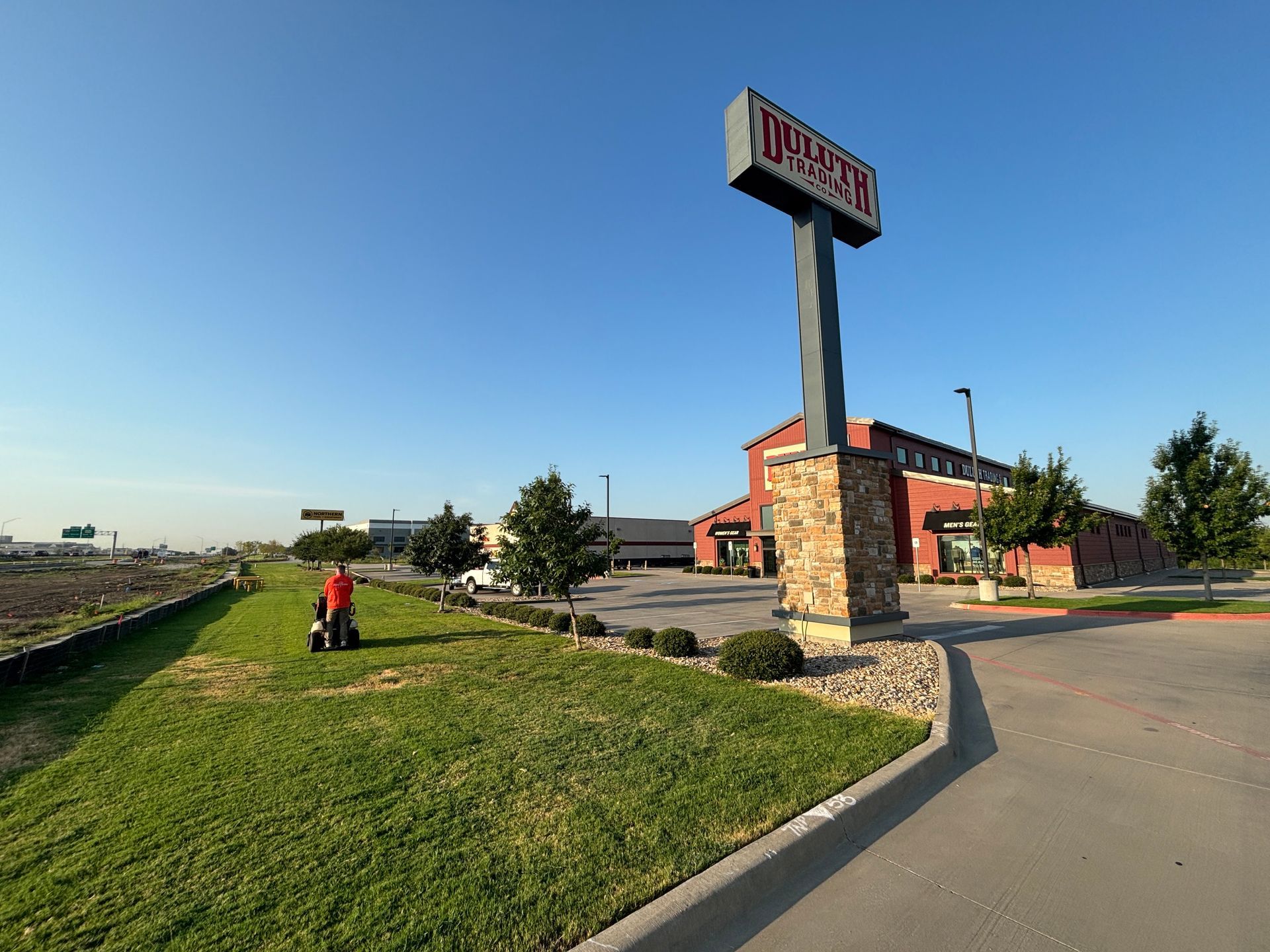 Wide roadside view of a Motel 6 sign, parking lot, and grassy verge under a clear blue sky