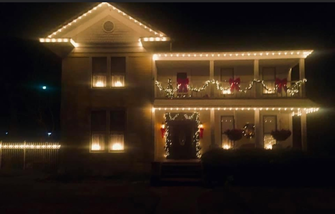House outlined with warm white Christmas lights at night, with decorated windows and porch.