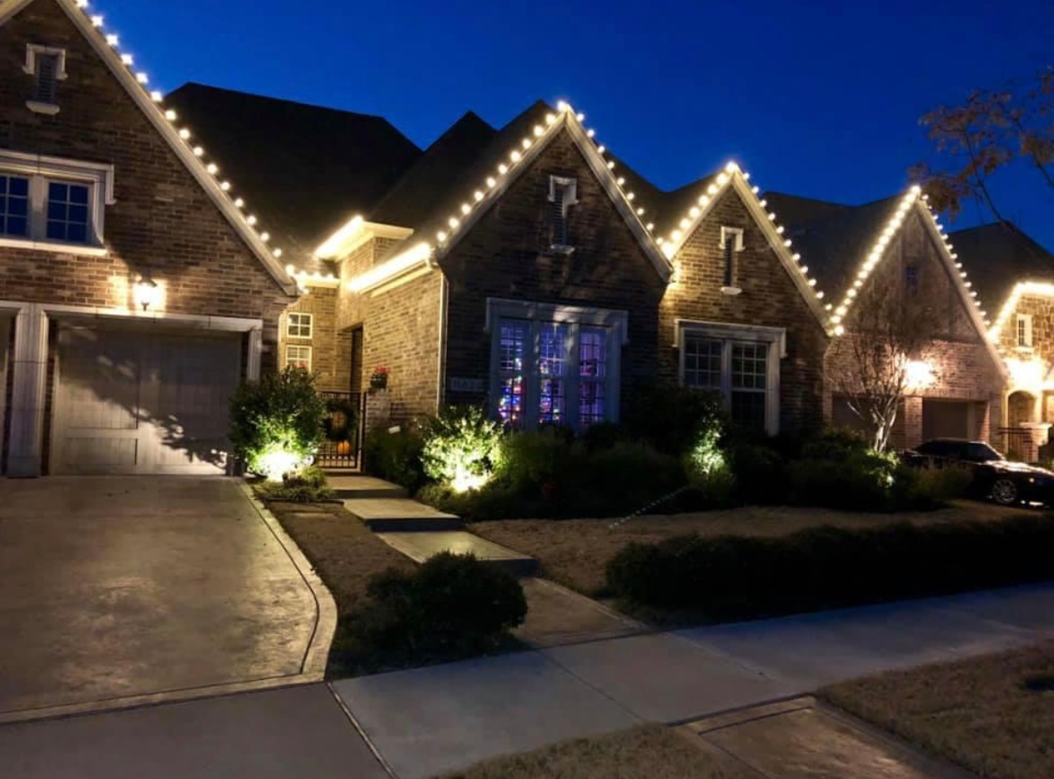 Brick house at night outlined with warm white Christmas lights and glowing front garden lights