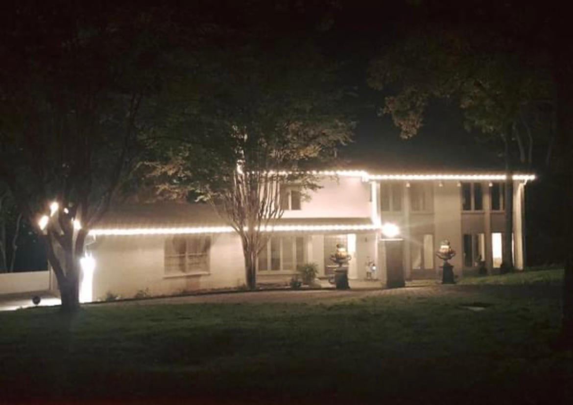 House lit up at night with porch lights and a large tree in front