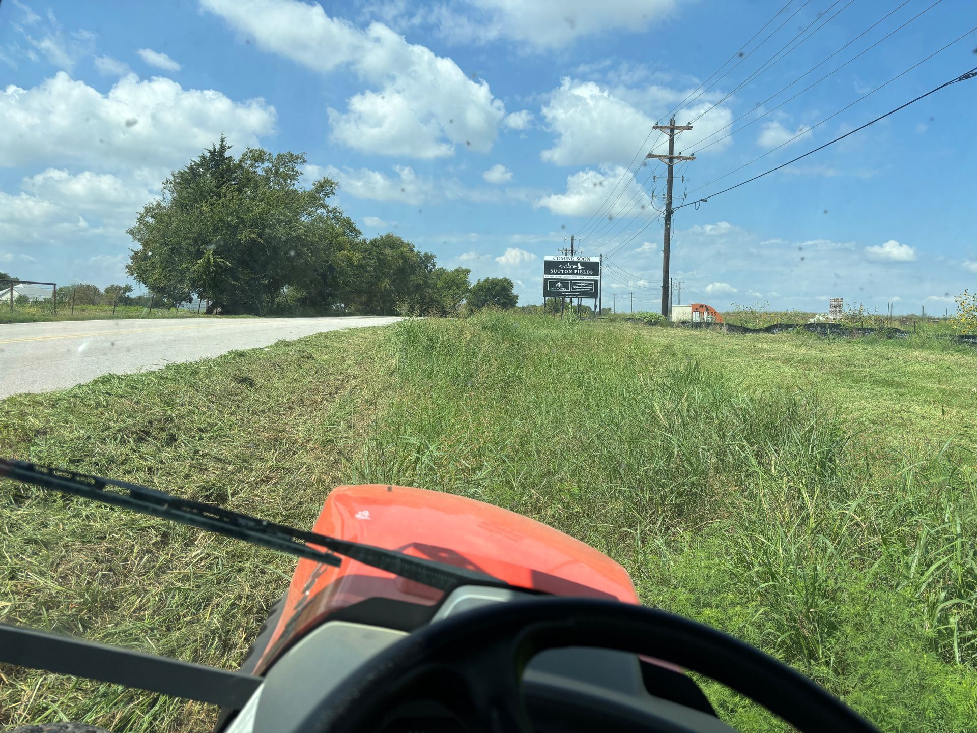 Lawn mower view beside a roadside grassy shoulder under a blue sky
