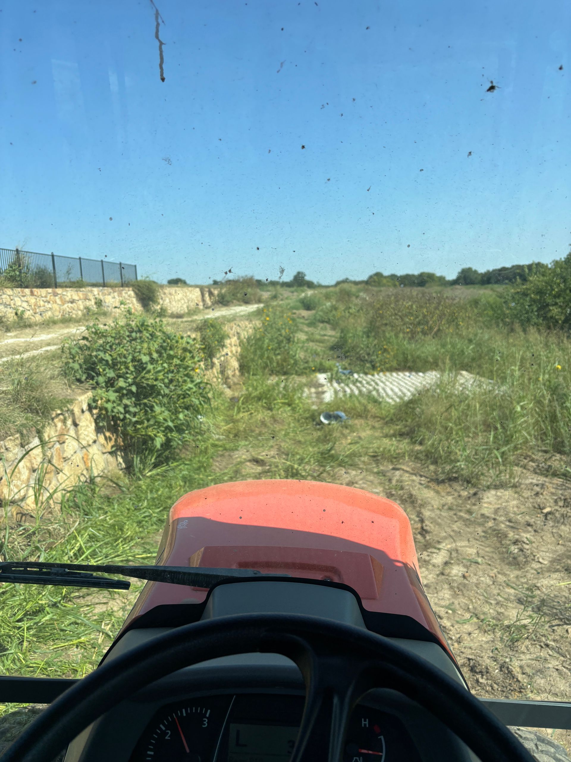 View from a tractor driving through a grassy field under a clear blue sky