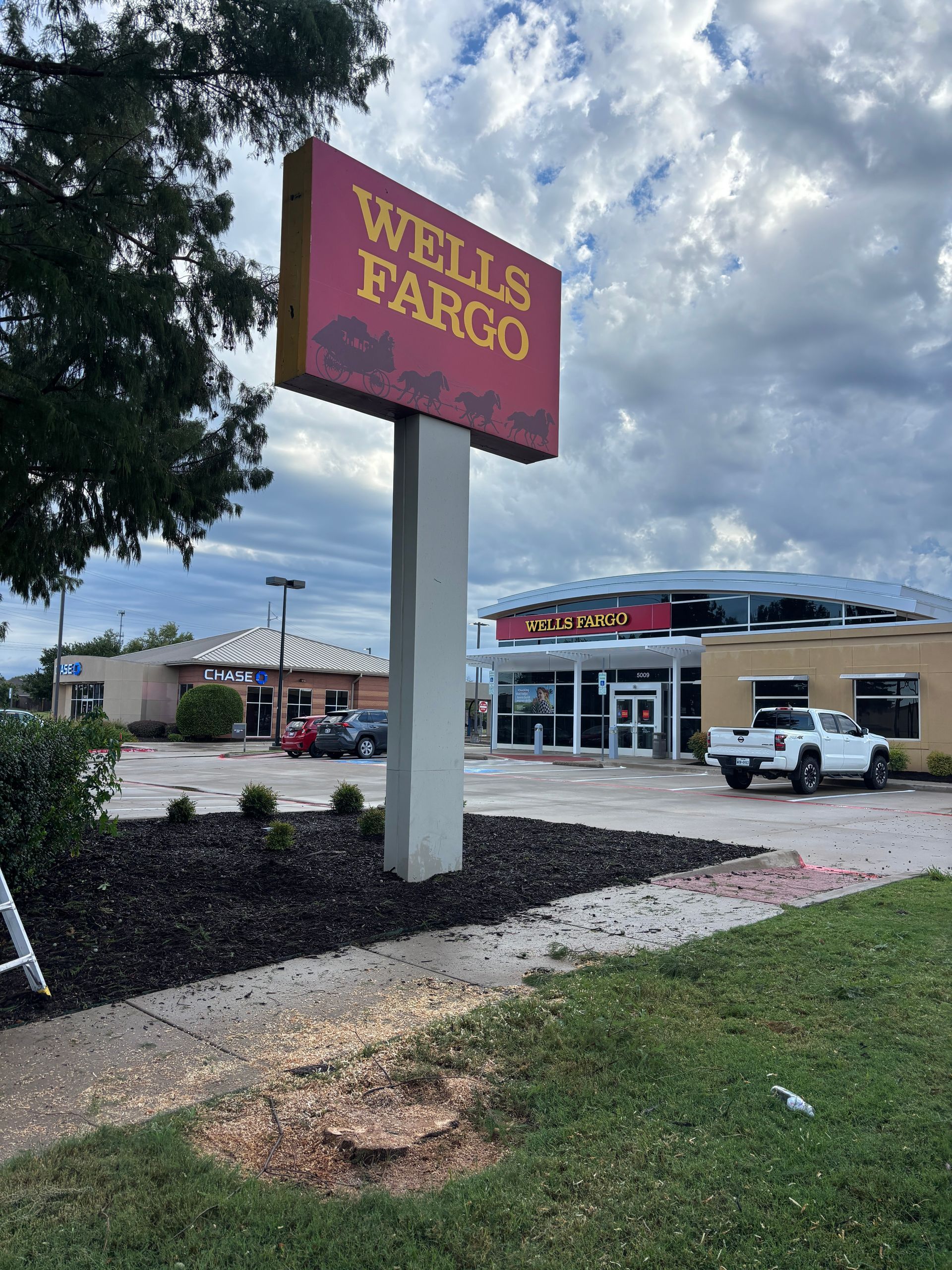 Wells Fargo branch sign in front of a bank building and parking lot on a cloudy day