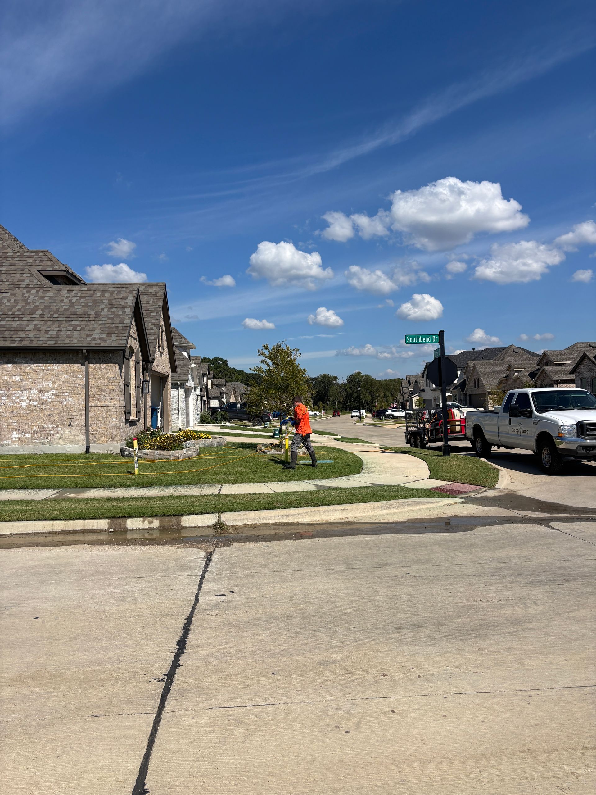 Suburban street with brick houses, a worker in orange, pickup truck, and bright blue sky with clouds