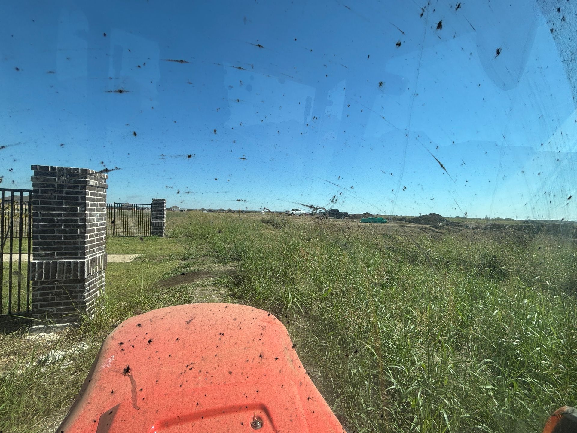 View from an orange tractor over a grassy field, with a stone gate pillar and blue sky.