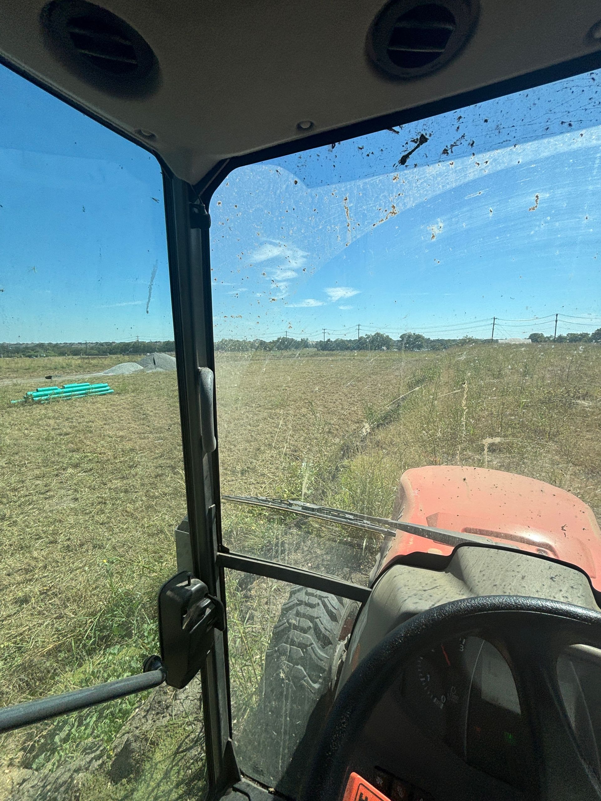 View from inside a tractor cab over a grassy field under a clear blue sky