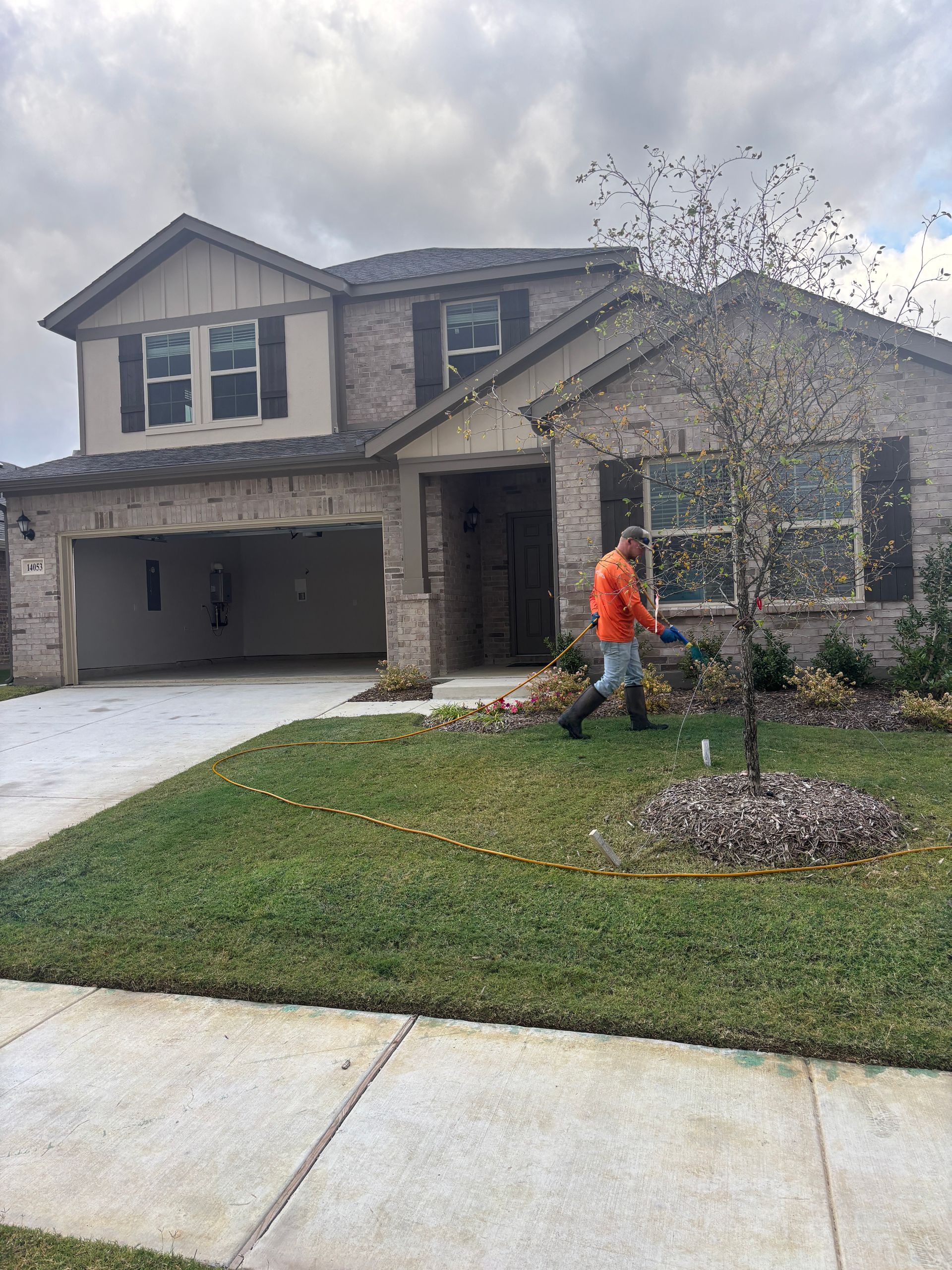 New house with stone facade and attached garage; worker in orange vest tends the front lawn.