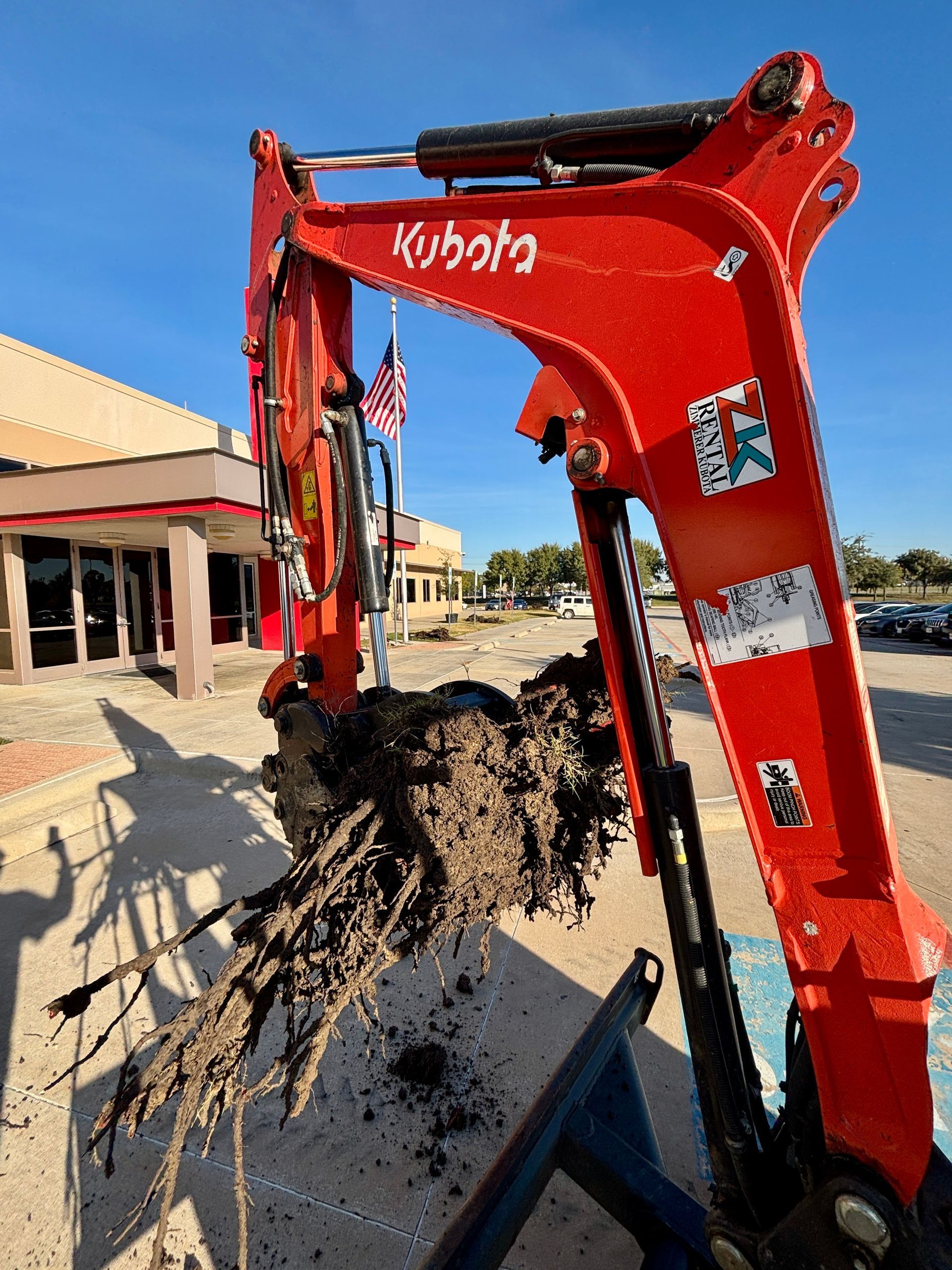 Red Kubota excavator digging dirt at a construction site beside a building