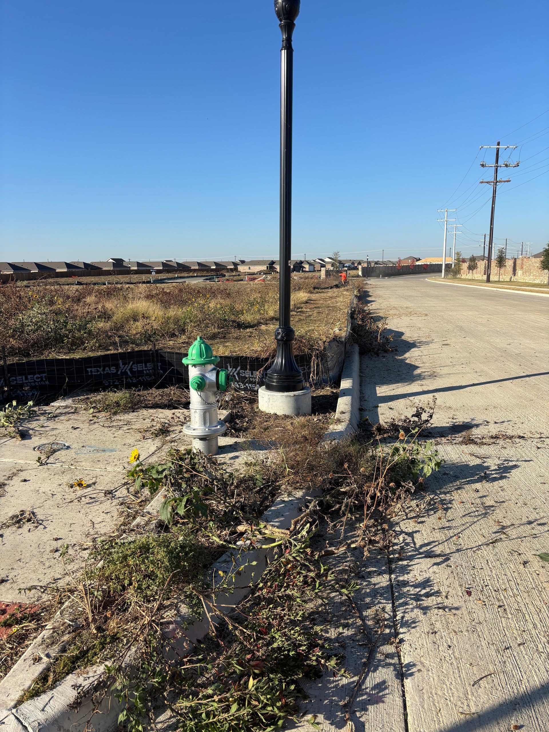 Utility pole and fire hydrant beside a gravel road, with dry brush and open field under a clear blue sky