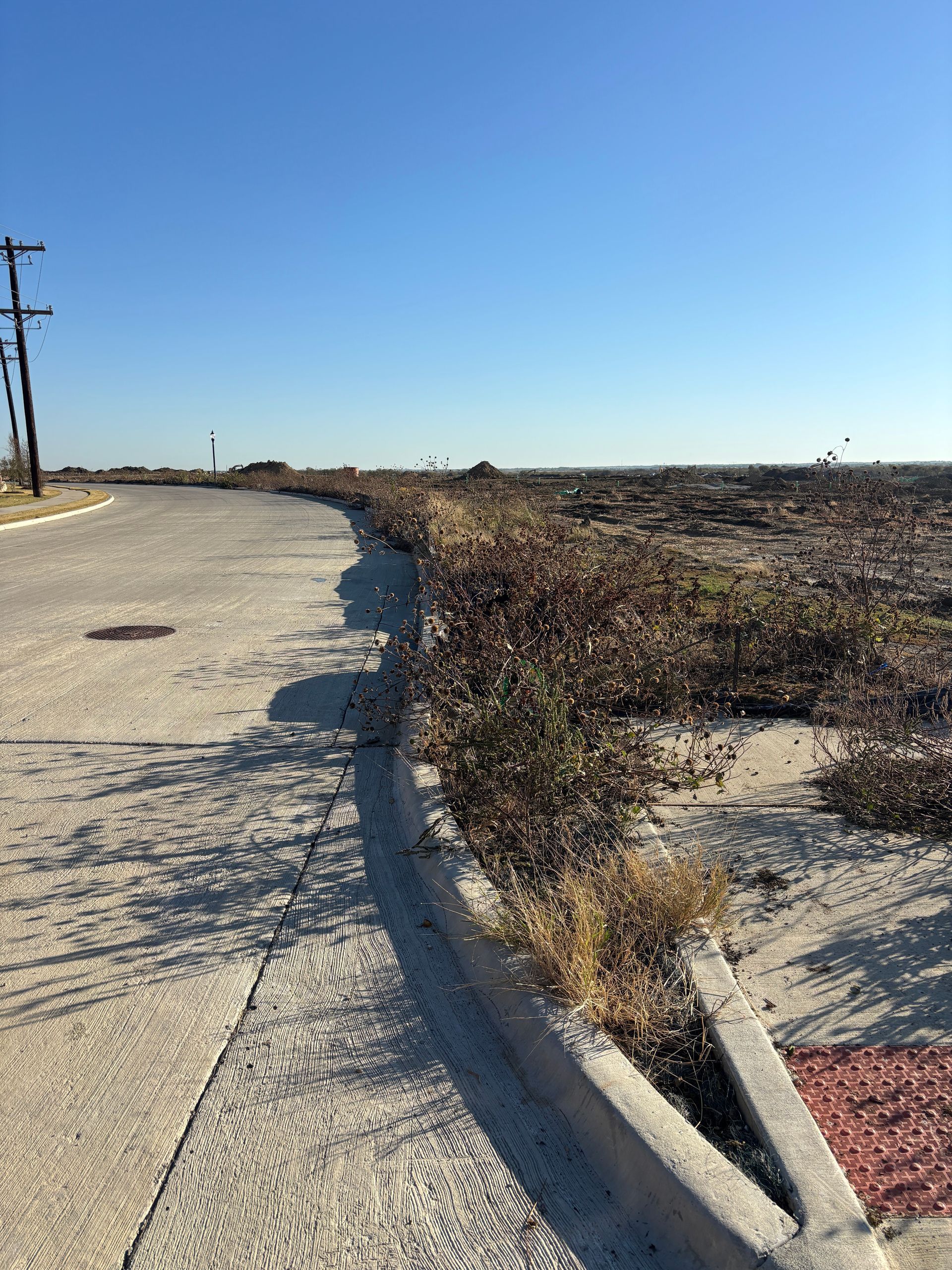 Curved sidewalk beside a dry, barren field under a clear blue sky