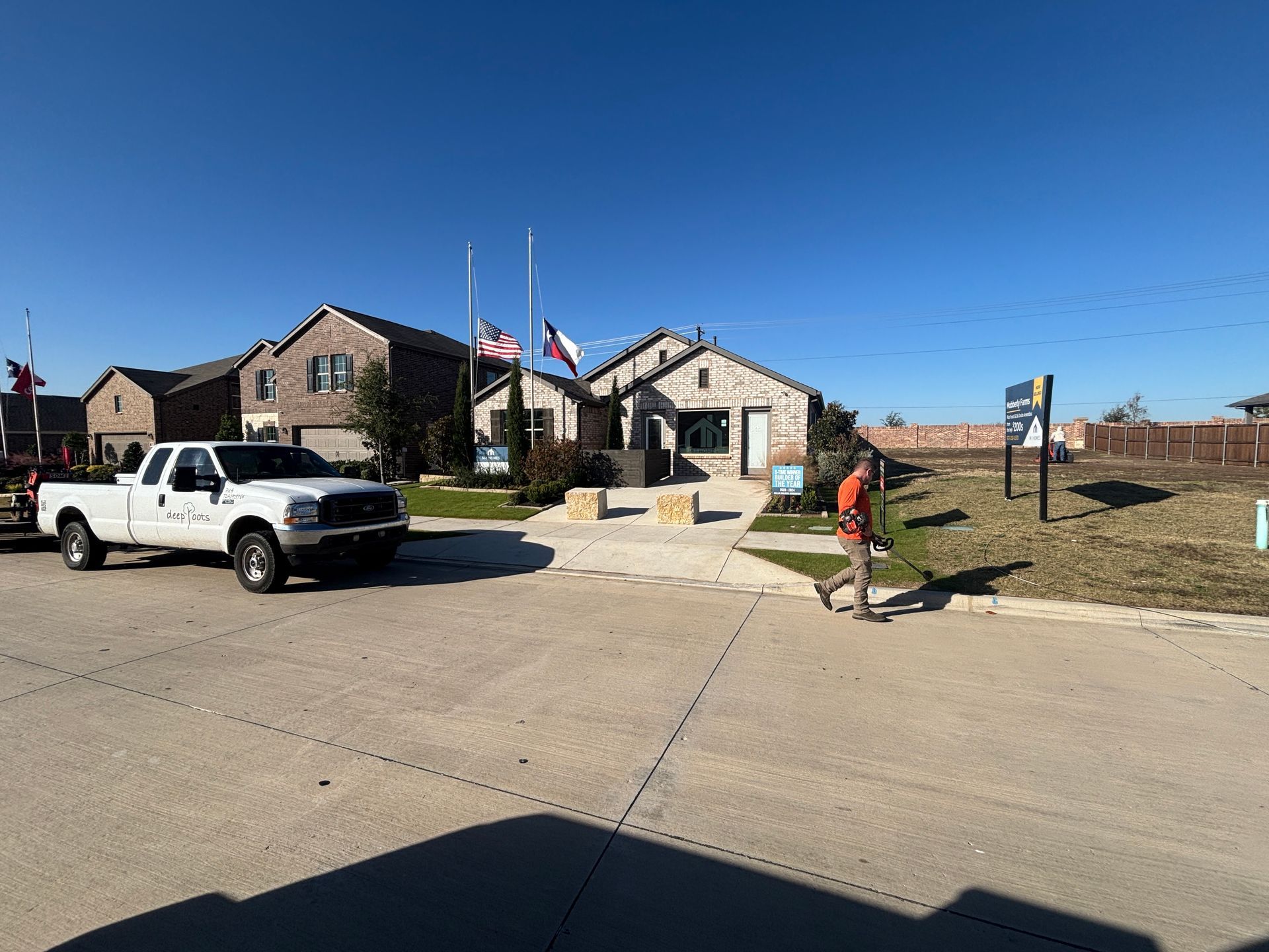 White pickup truck parked outside a brick building, with a person walking near a sign under a clear blue sky.