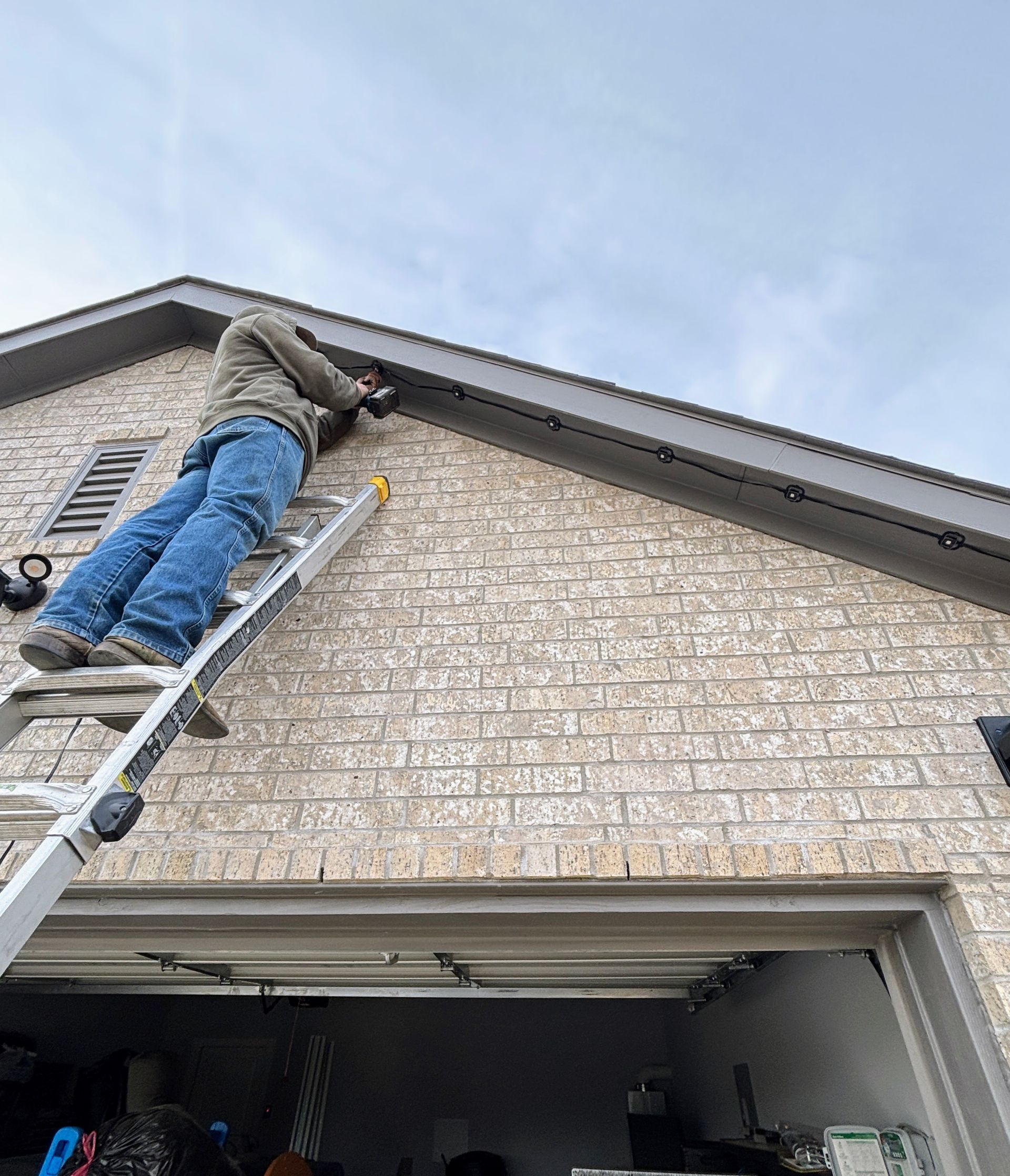 Worker on a ladder painting a house gable above an open garage.