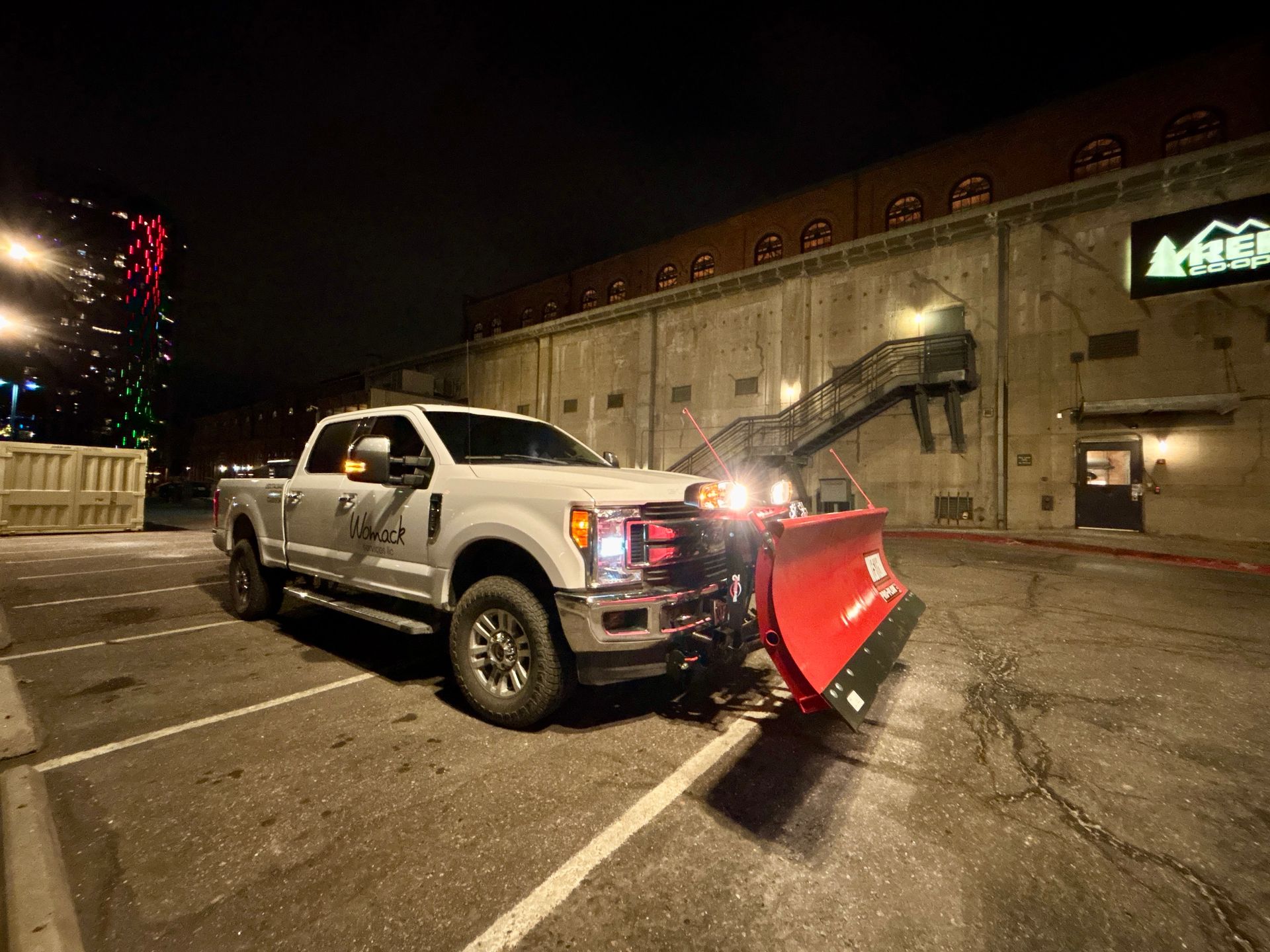 Pickup truck with red snowplow angled in an empty parking lot at night