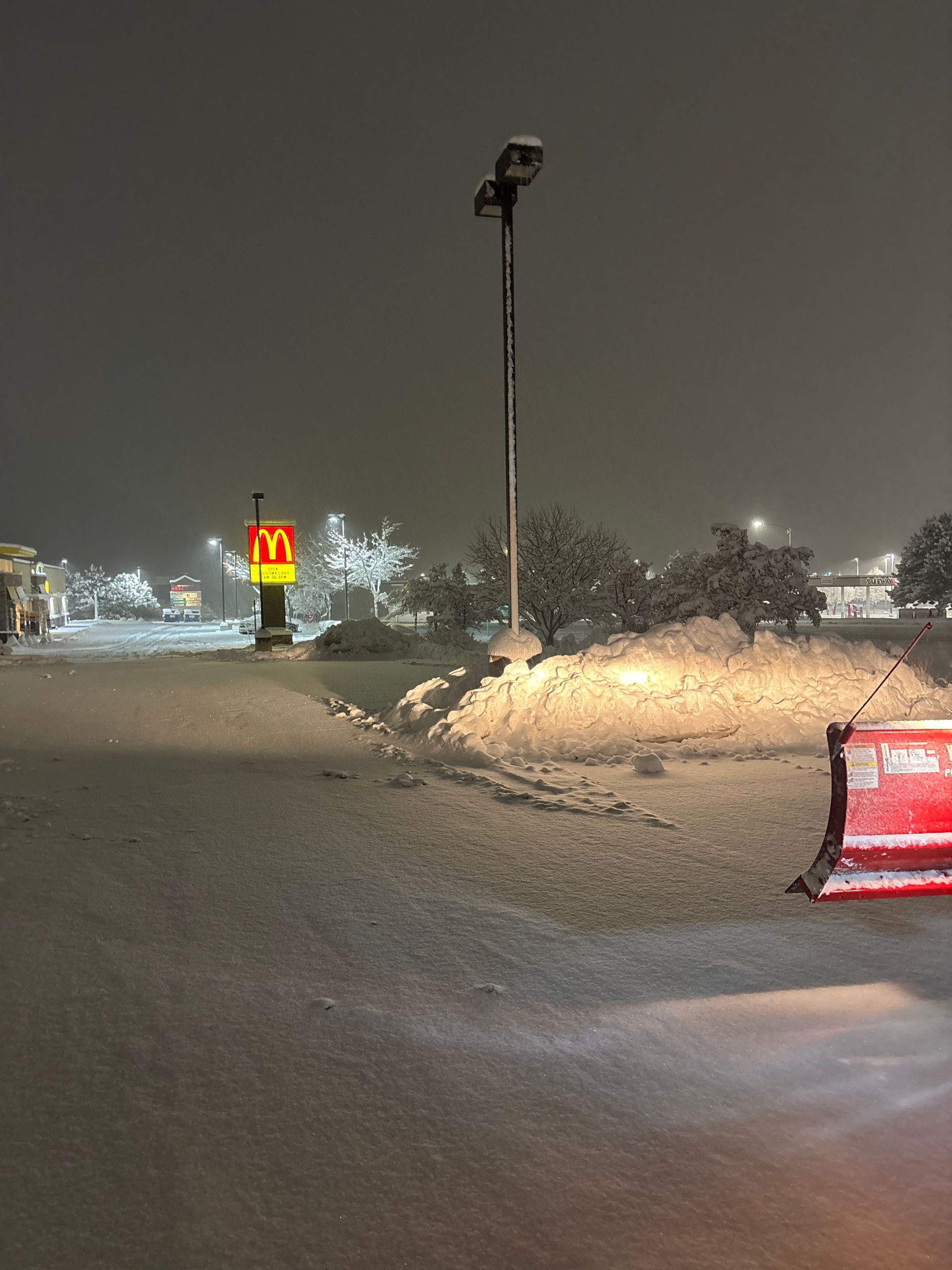 Snowy nighttime street with a McDonald’s sign, tall lamp post, and a partially buried red barrier.