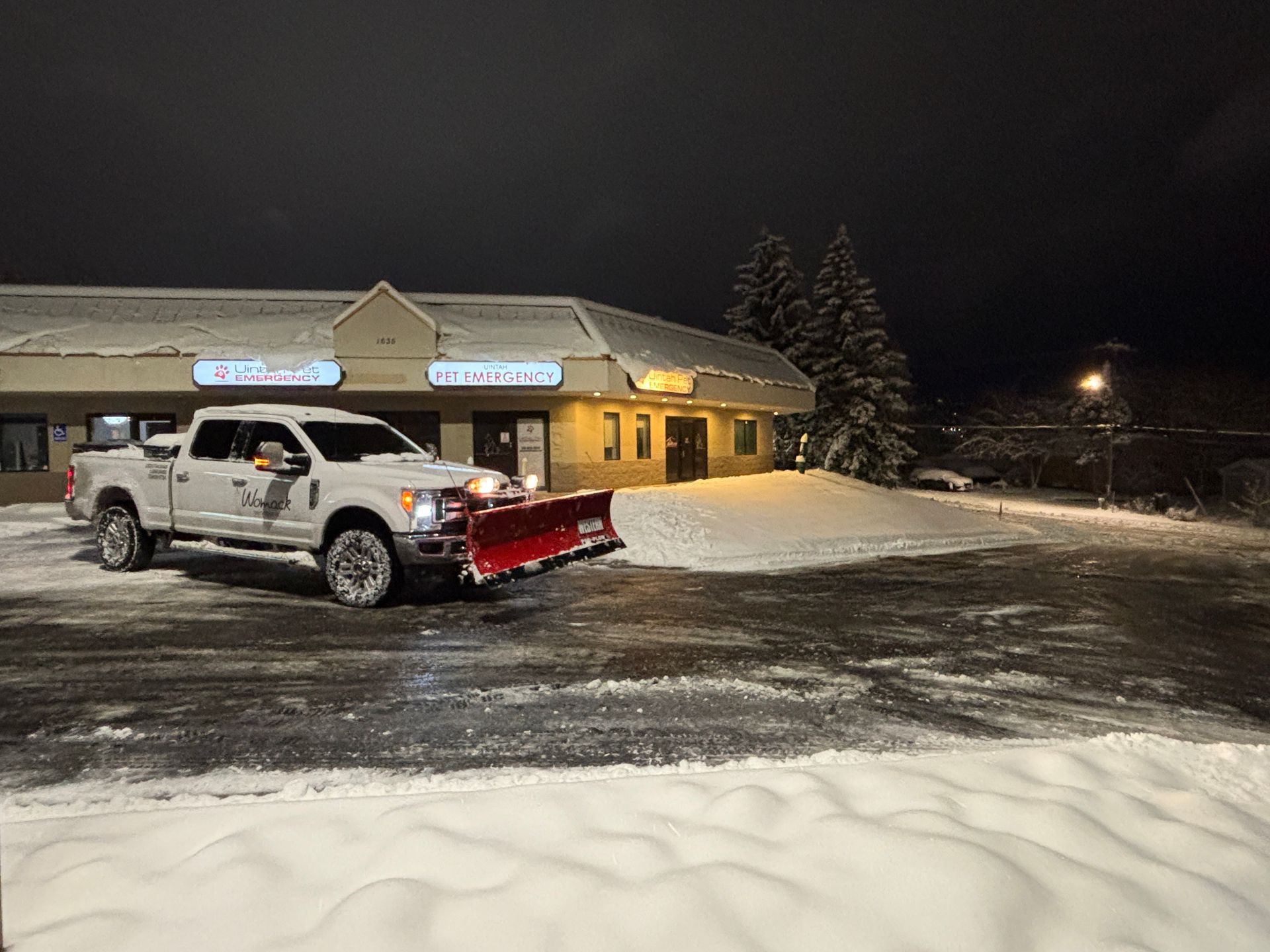 Snow-covered white pickup truck in front of a lit building at night