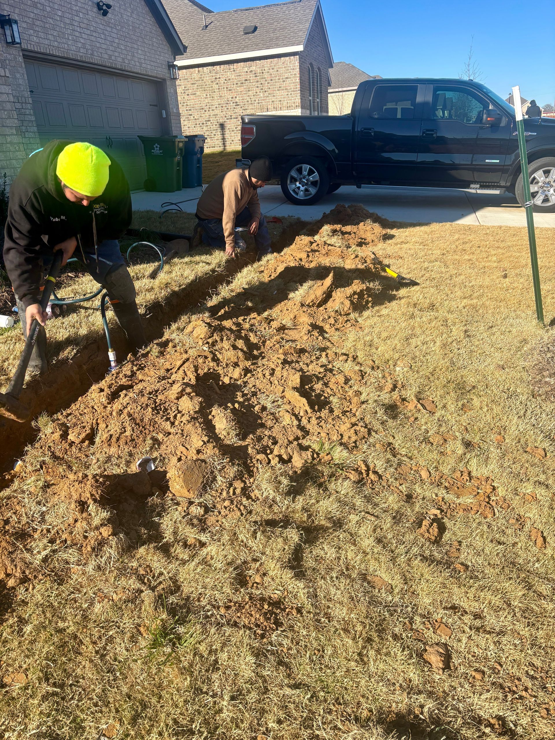 Person working in a yard beside a large pile of leaves, with a pickup truck parked nearby.