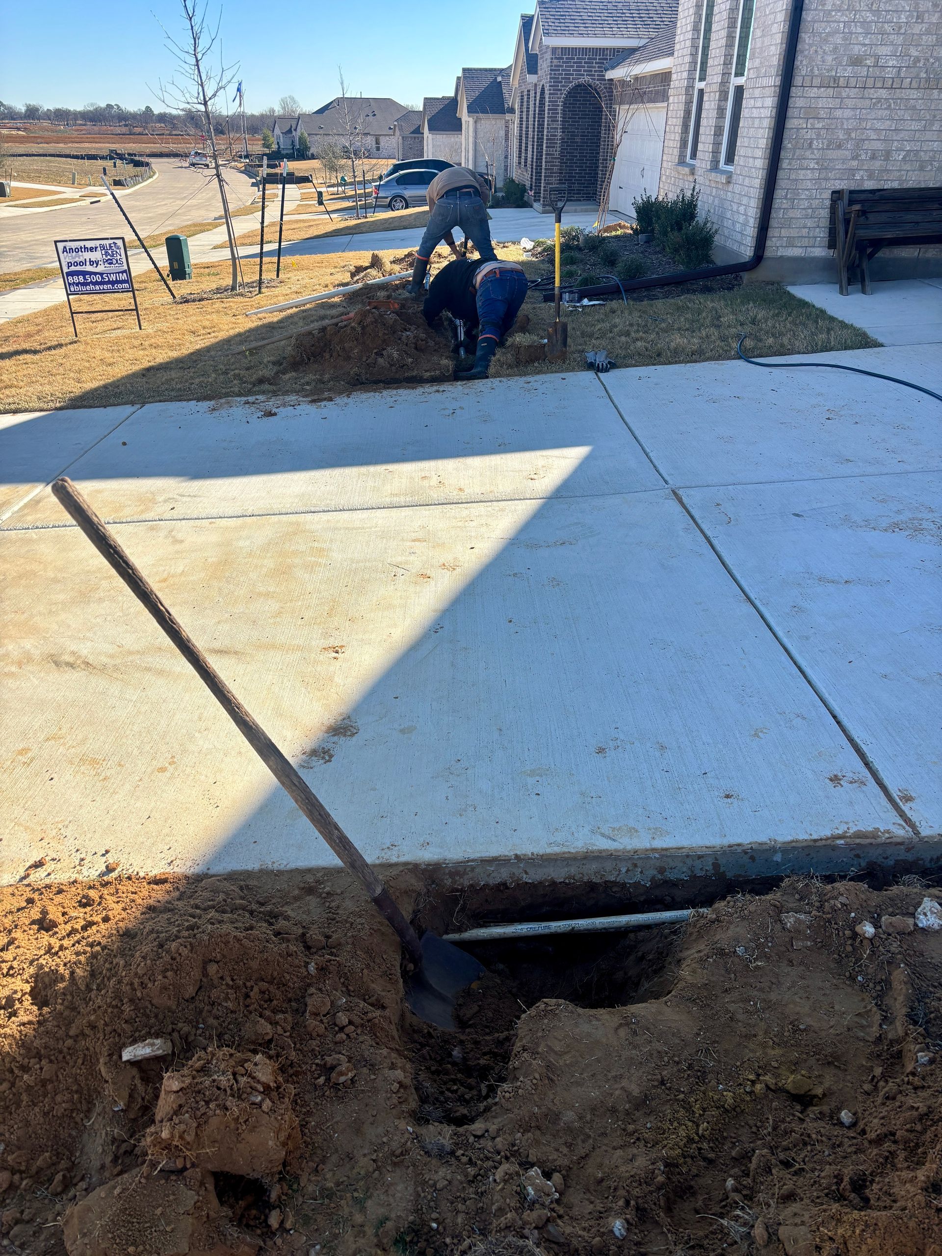 Damaged sidewalk with a large hole and exposed soil beside a house under construction.