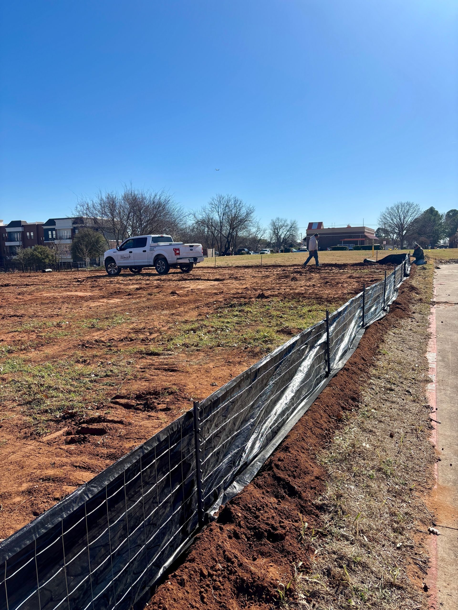 Construction site with white truck, workers, and black silt fencing under a clear blue sky