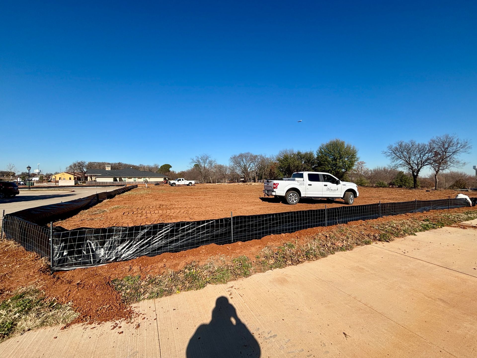 White pickup truck parked on a dirt lot with black silt fencing under a clear blue sky