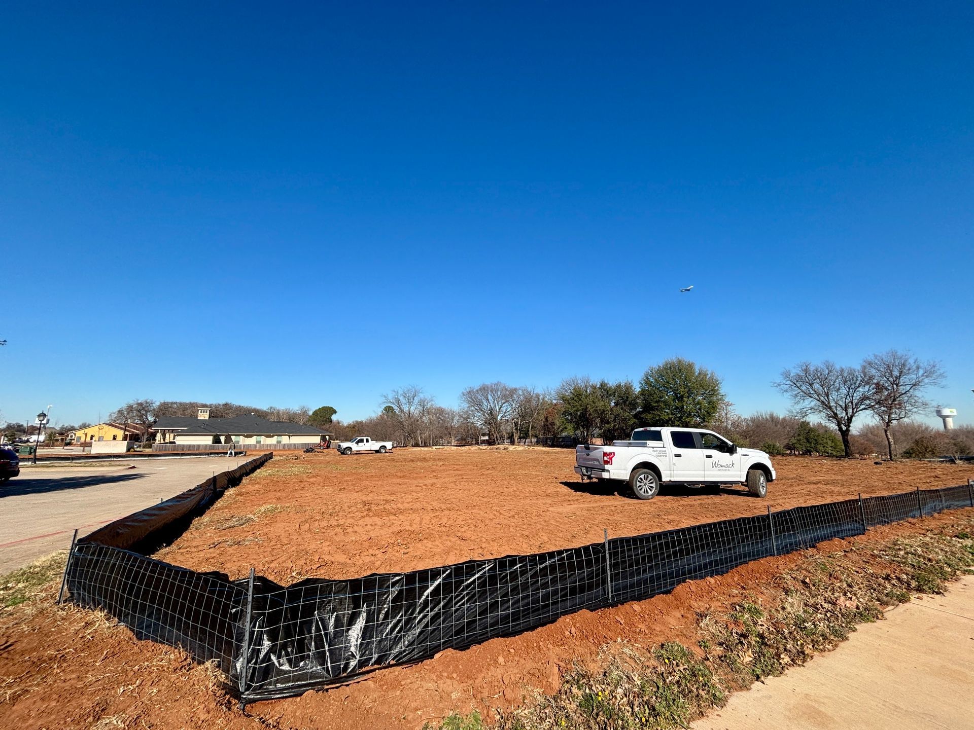 White SUV parked beside a large mulch-covered raised bed under a clear blue sky