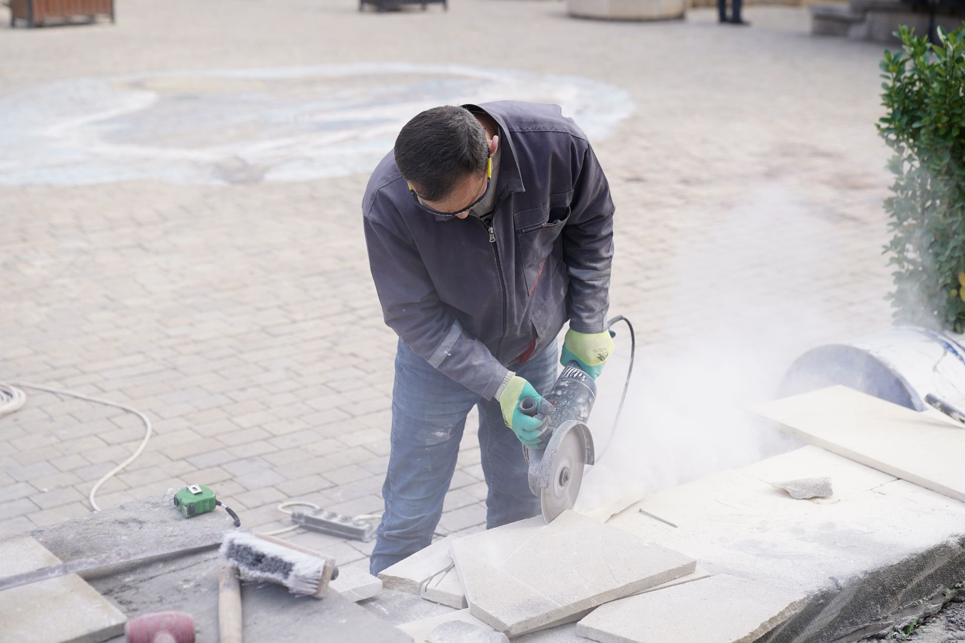 Worker cutting stone slab with a power saw, creating a cloud of dust outdoors.