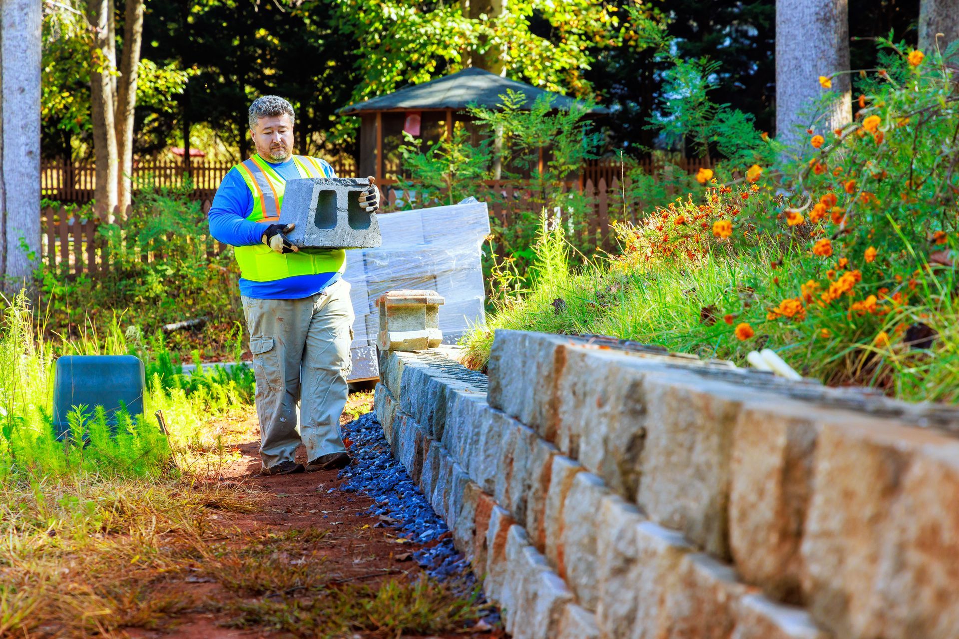Worker in a neon vest inspecting a stone wall in a sunny garden path