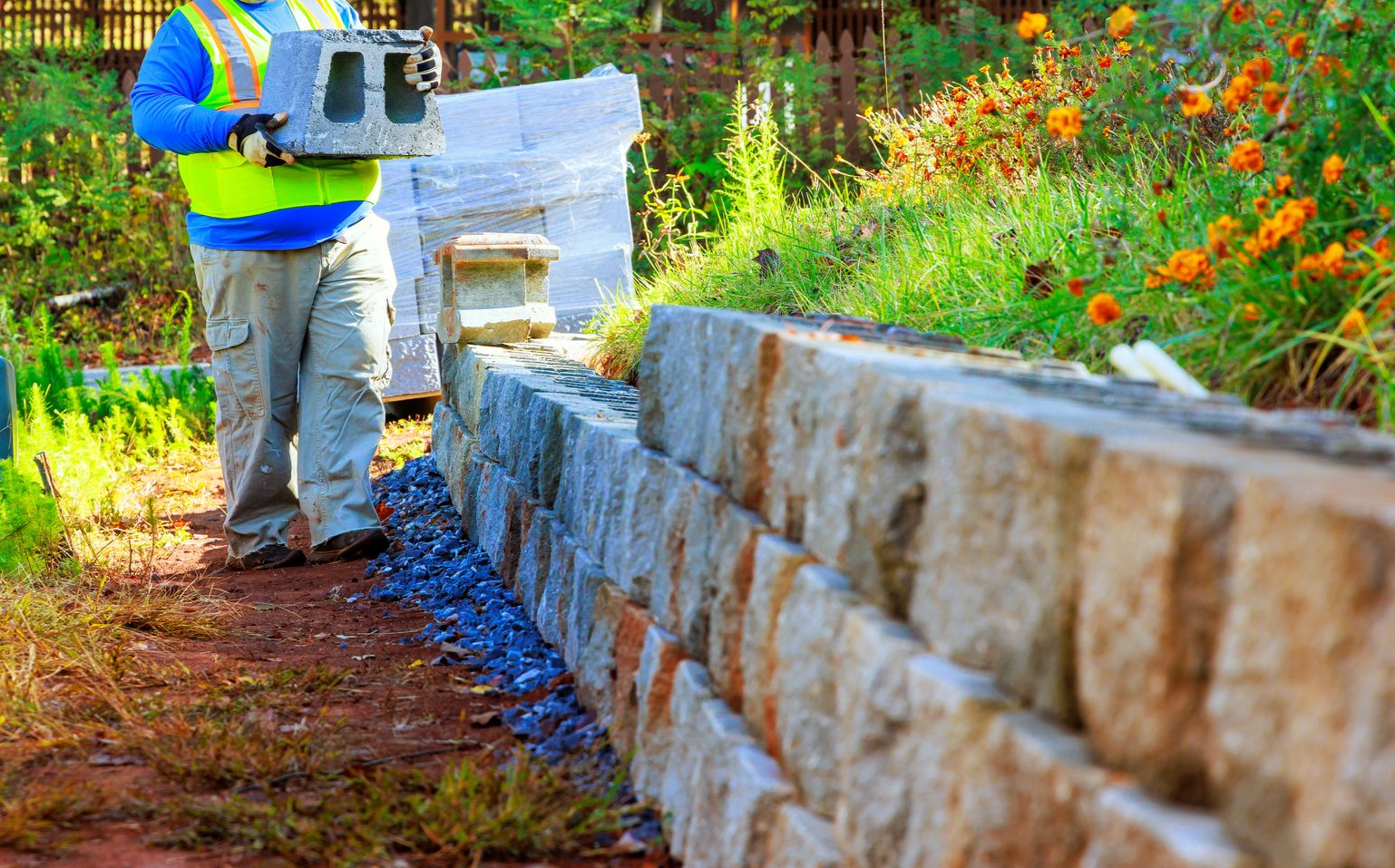 Worker in a safety vest laying a stone retaining wall beside a garden path