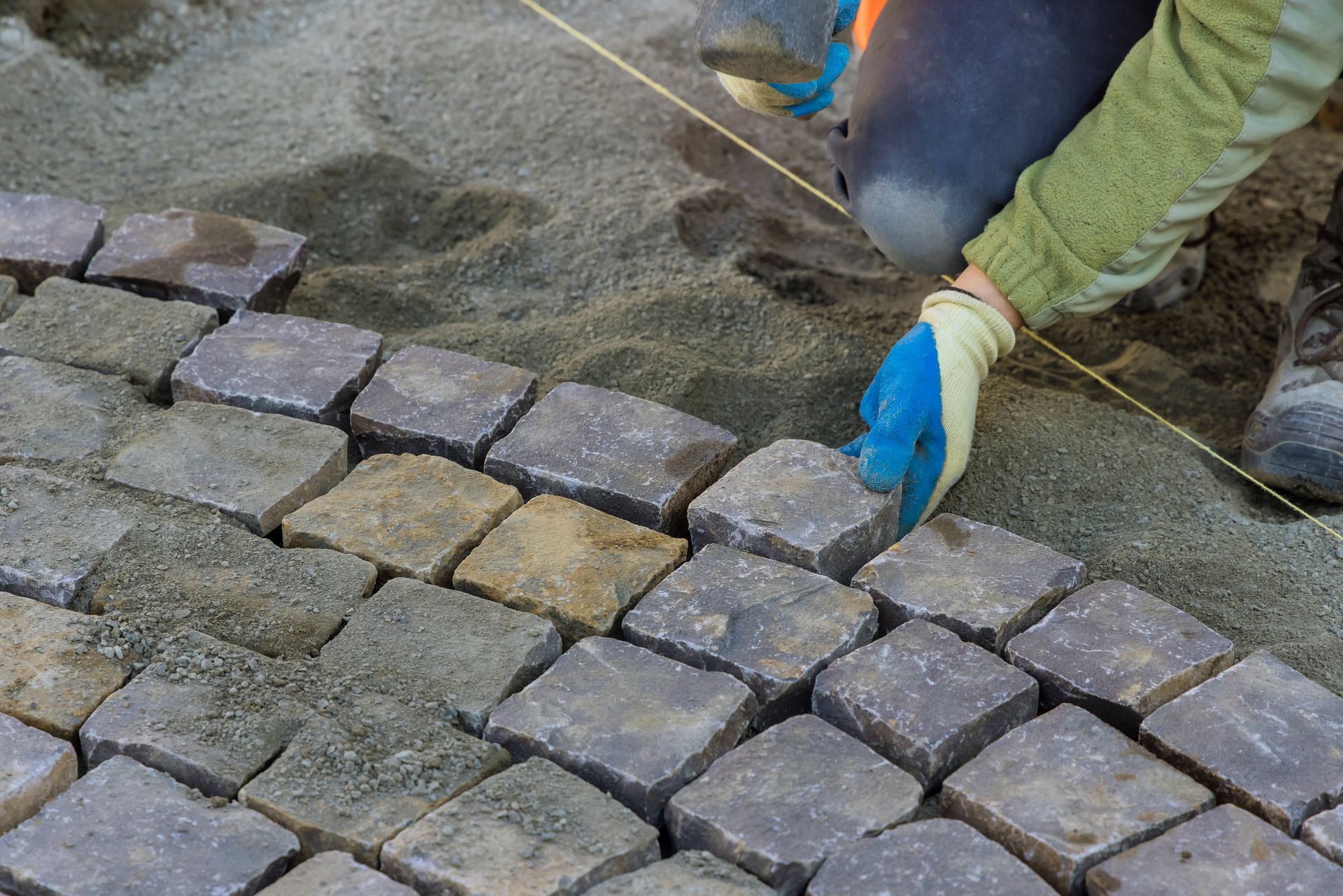 Worker in blue gloves placing cobblestones into a paved walkway.