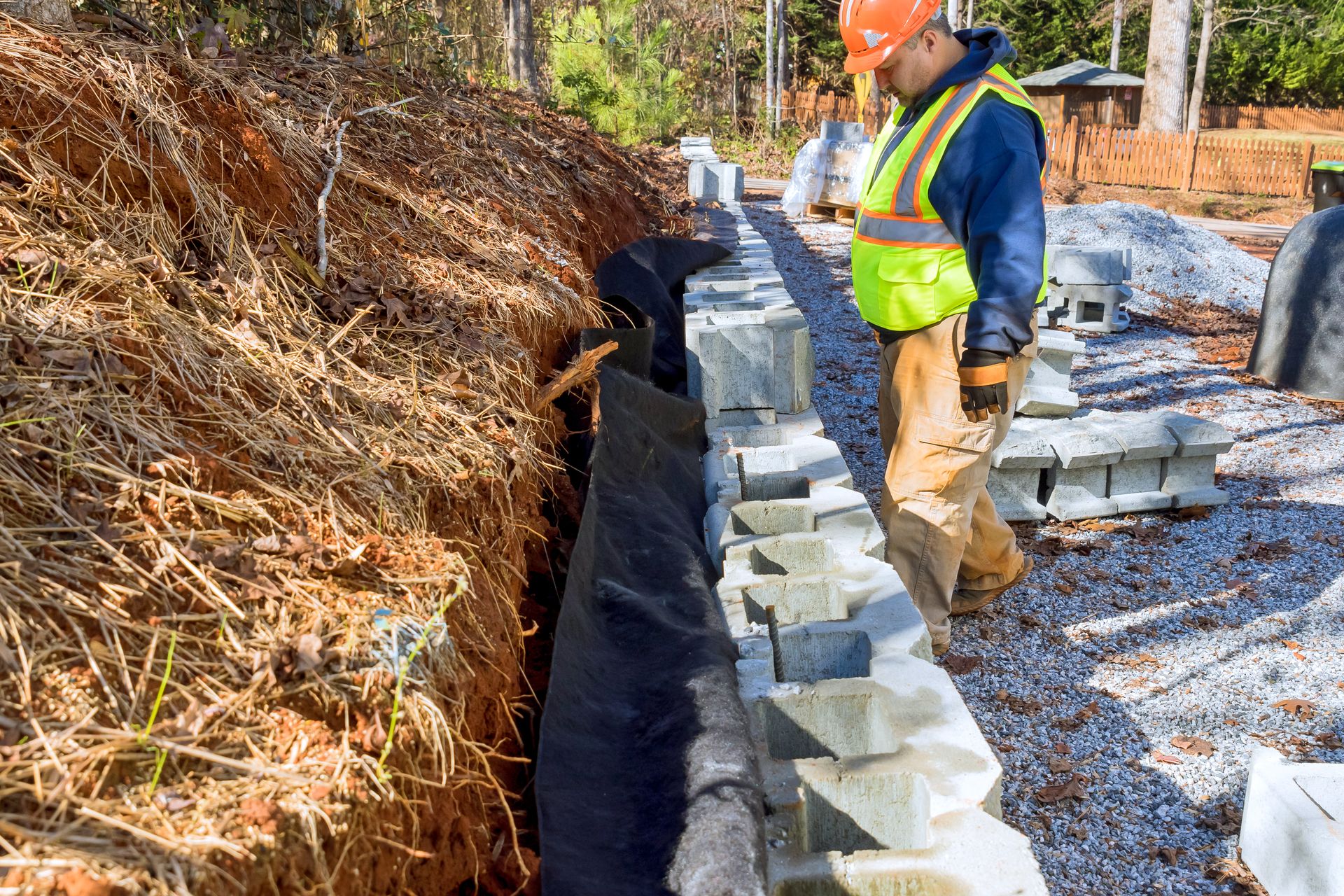Worker in safety vest stacking concrete blocks beside a trench at a construction site