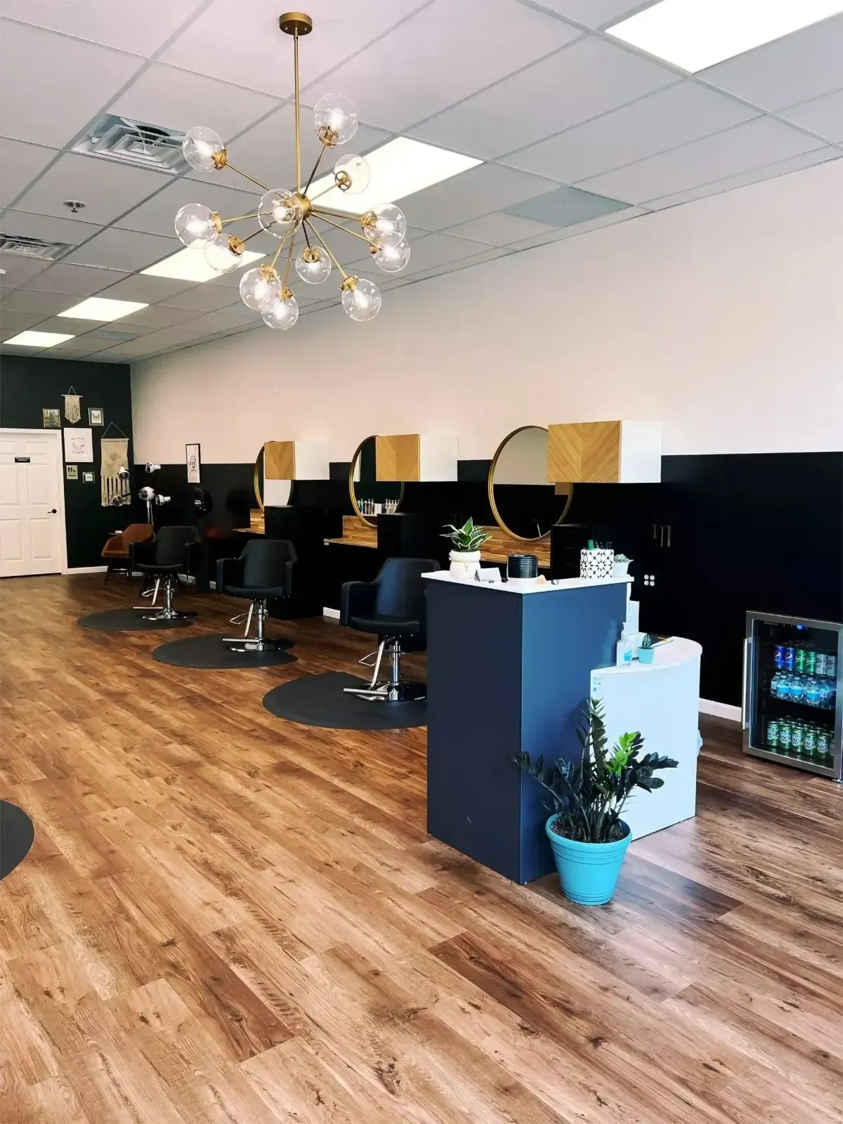 Modern hair salon interior with styling chairs, mirrors, wood flooring, and a small plant display