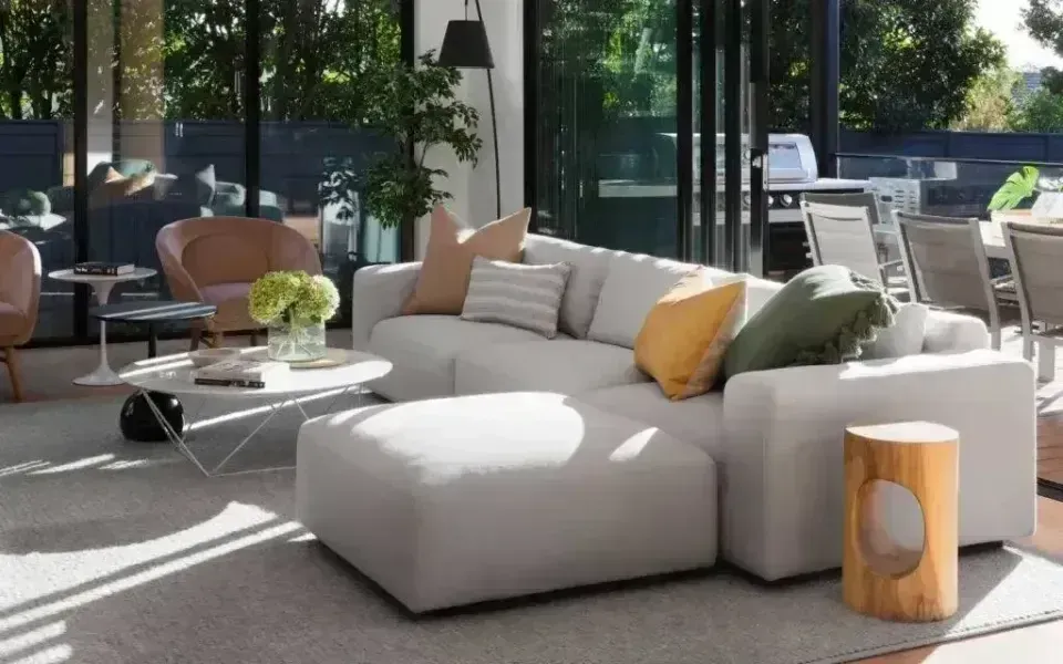 Bright modern living room with white sectional sofa, glass coffee table, and large windows opening to a patio.