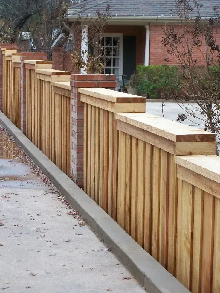 Wooden fence lining a sidewalk beside a brick house and driveway in a residential neighborhood