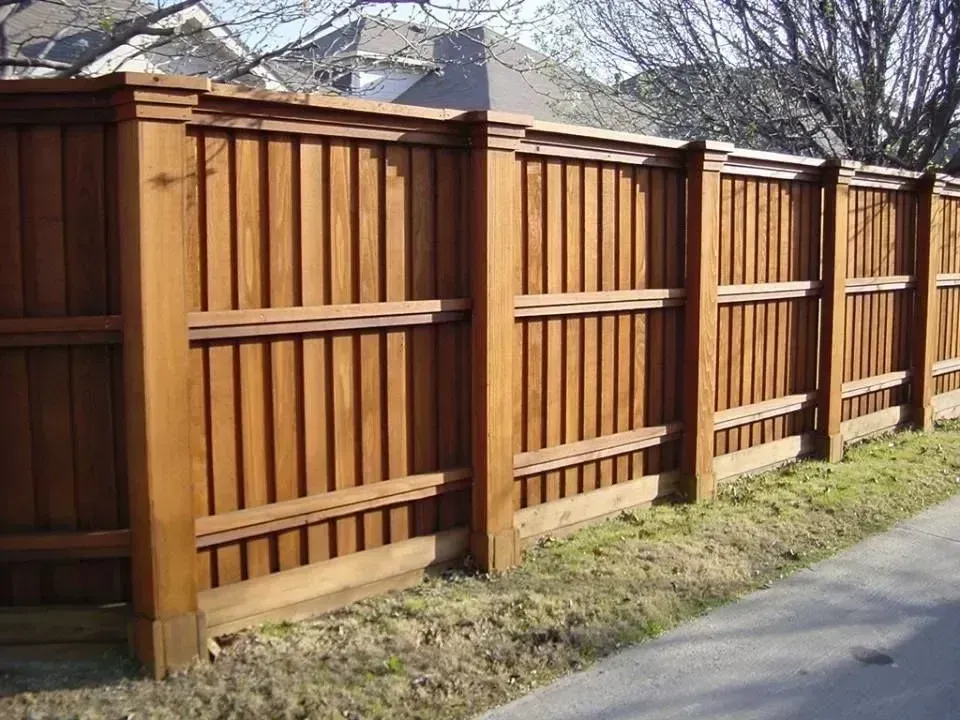 Wooden privacy fence along a sidewalk beside a grassy yard under a bright sky