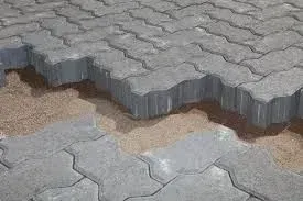 Buckled gray paving stones lifted by erosion, exposing sand beneath a damaged walkway.