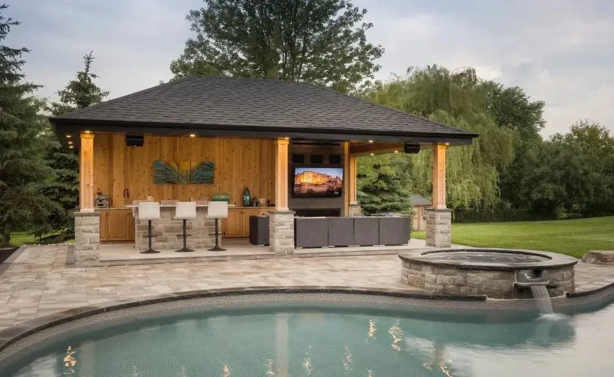 Backyard pool with a stone patio and a small wooden pavilion at dusk