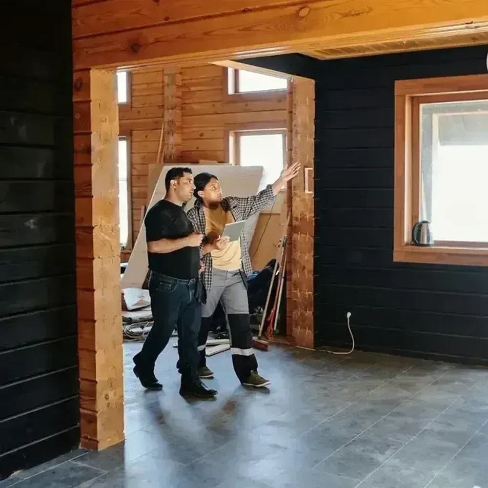 Two people discussing wall layout inside a wooden room under construction