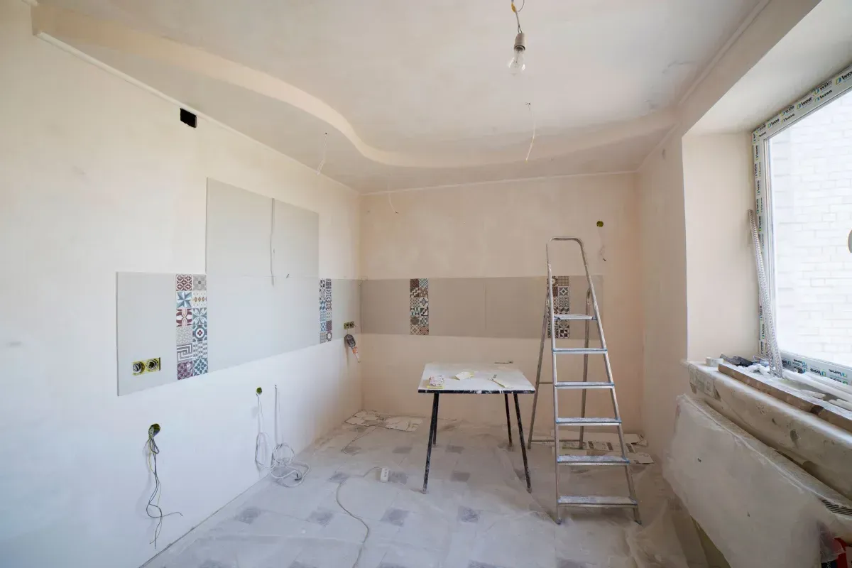 Unfinished room with white walls, ladder, work table, and large window during renovation.