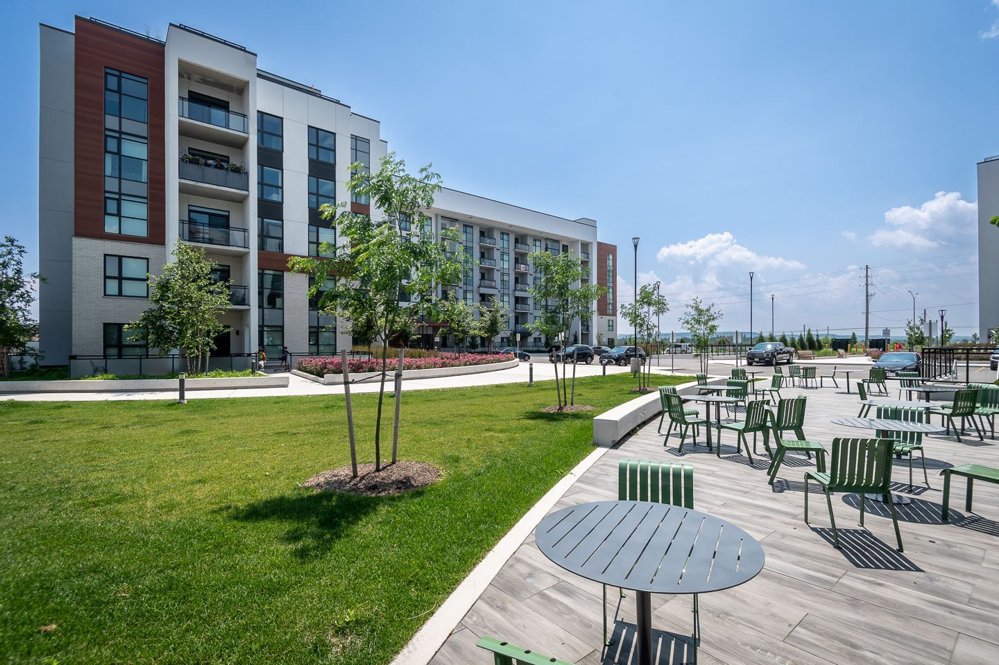 Modern apartment building with a green lawn and outdoor patio seating under a clear blue sky