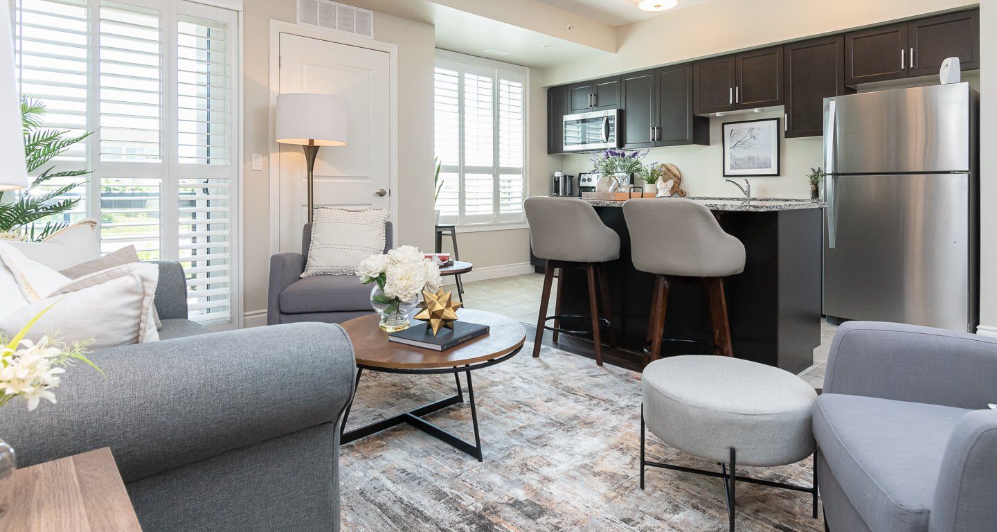 Bright modern living room with gray sofa, rug, round coffee table, and adjacent kitchen with bar stools.