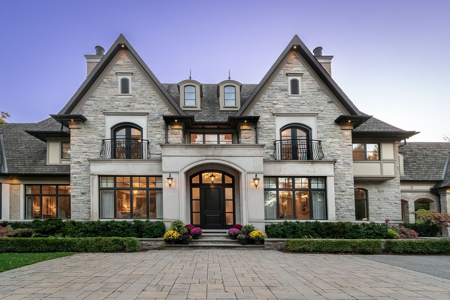Large stone mansion with arched windows, a central entryway, and manicured landscaping at dusk
