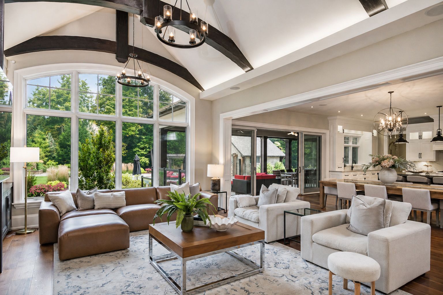 Bright modern living room with large windows, white sofas, leather ottoman, and neutral decor