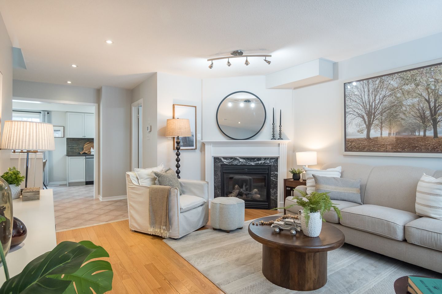 Bright living room with fireplace, beige sofa, round mirror, and open kitchen in the background.