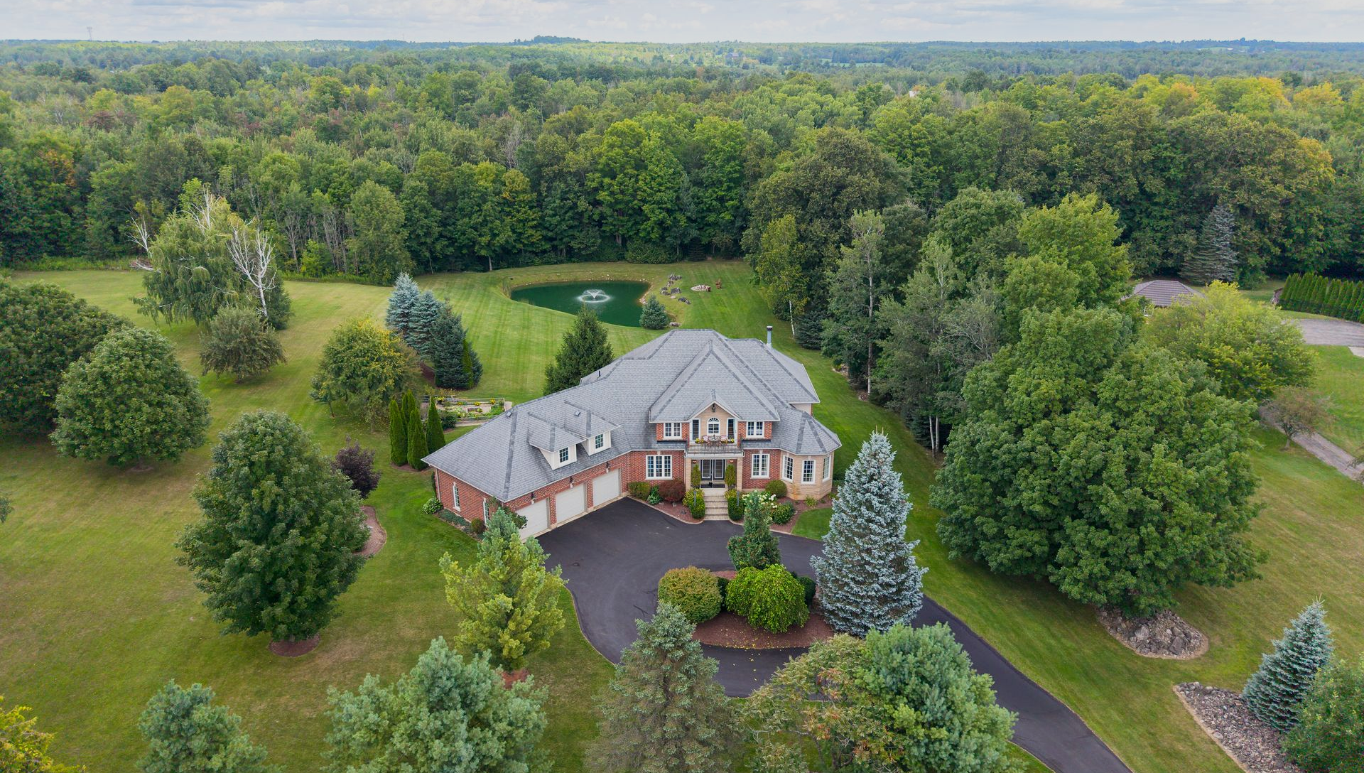 Aerial view of a large suburban house with a curved driveway, surrounded by lush green trees and lawn.