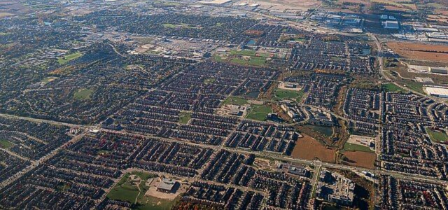 Aerial view of a suburban neighborhood with rows of houses, trees, and green spaces.