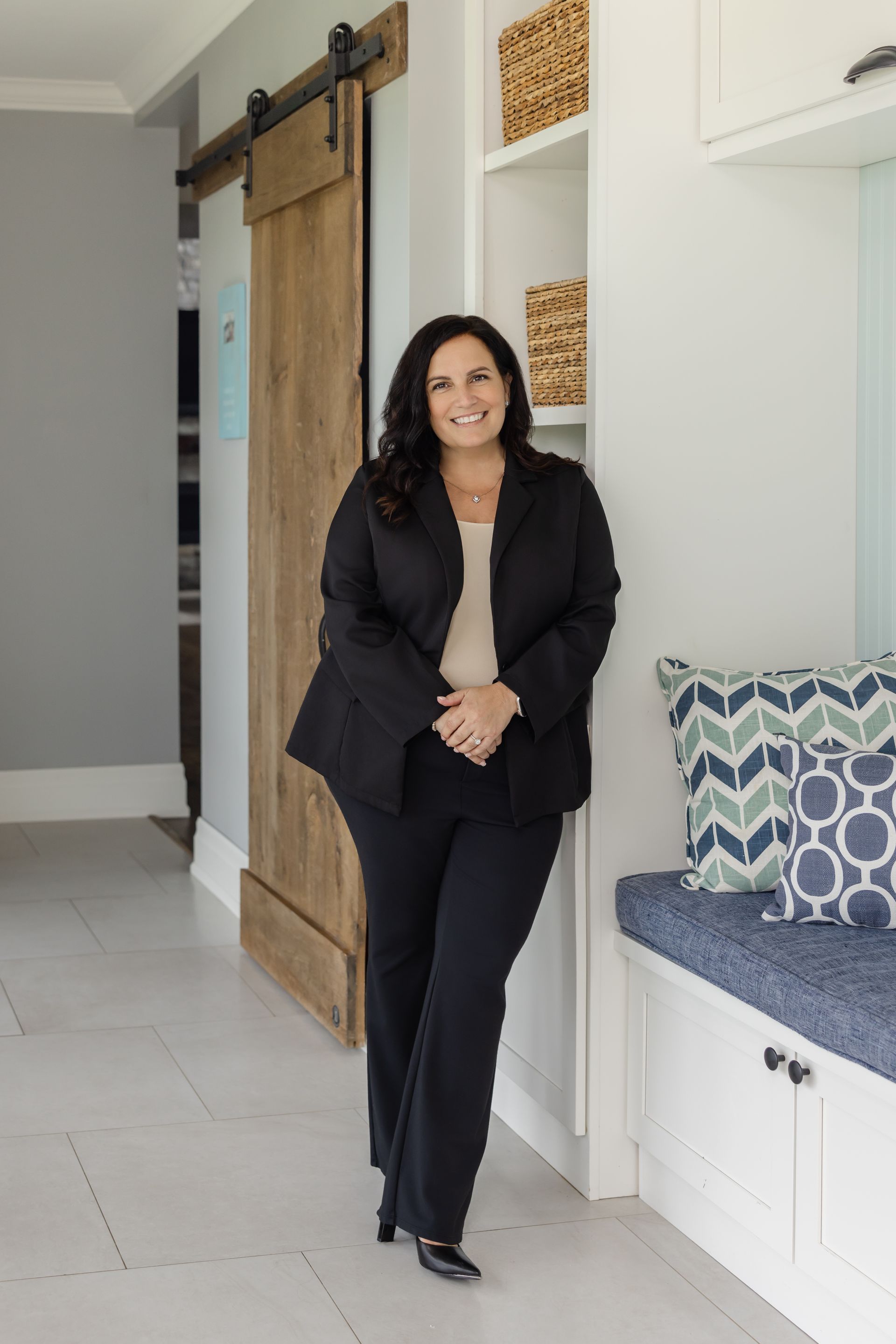 Woman with dark hair smiles in white kitchen, leaning on counter.