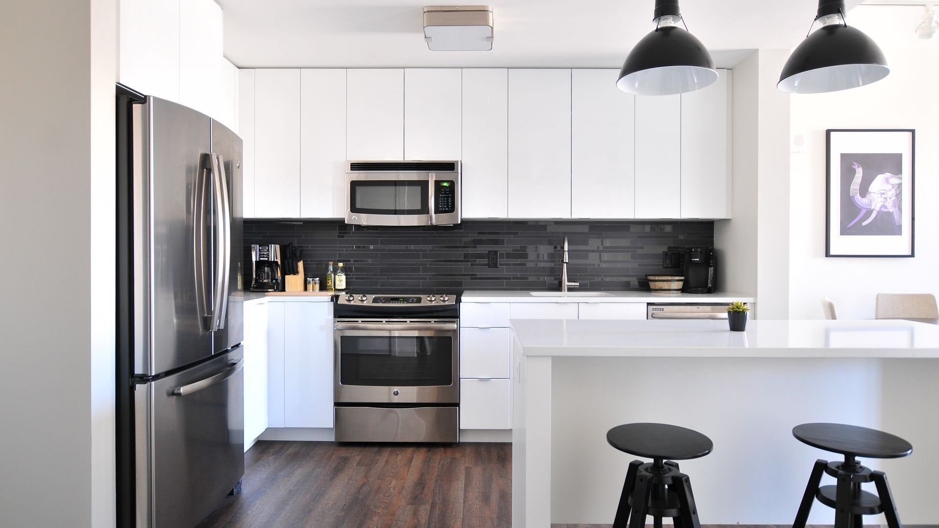 A kitchen with white cabinets , stainless steel appliances , a refrigerator and a microwave.