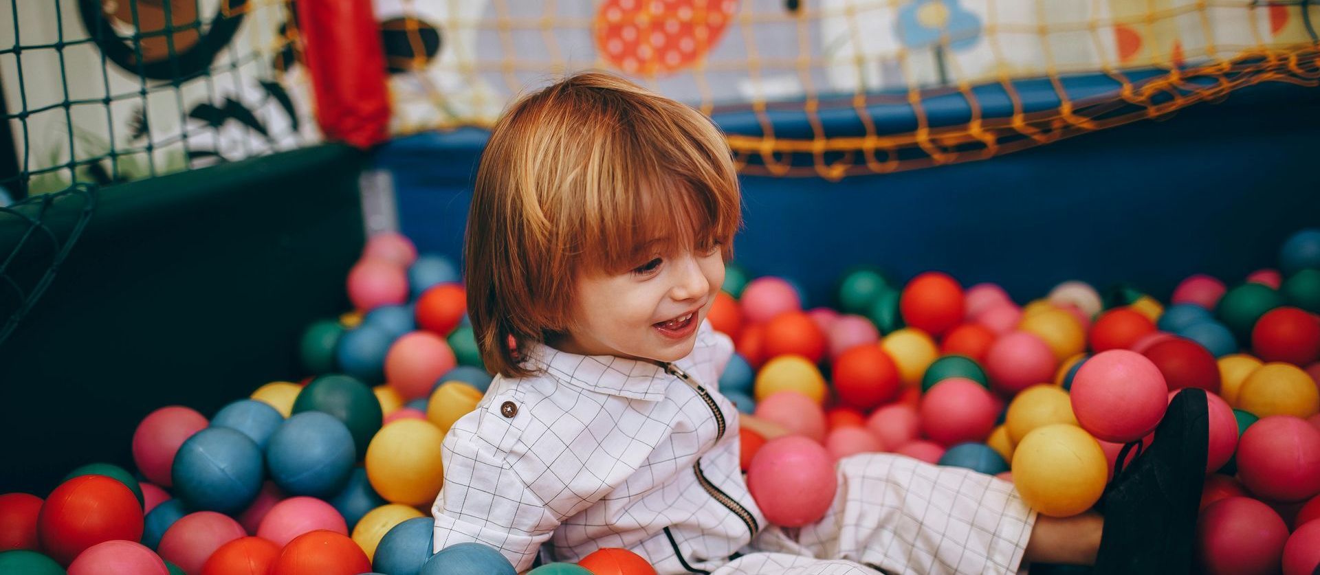 A little girl is sitting in a ball pit filled with colorful balls.