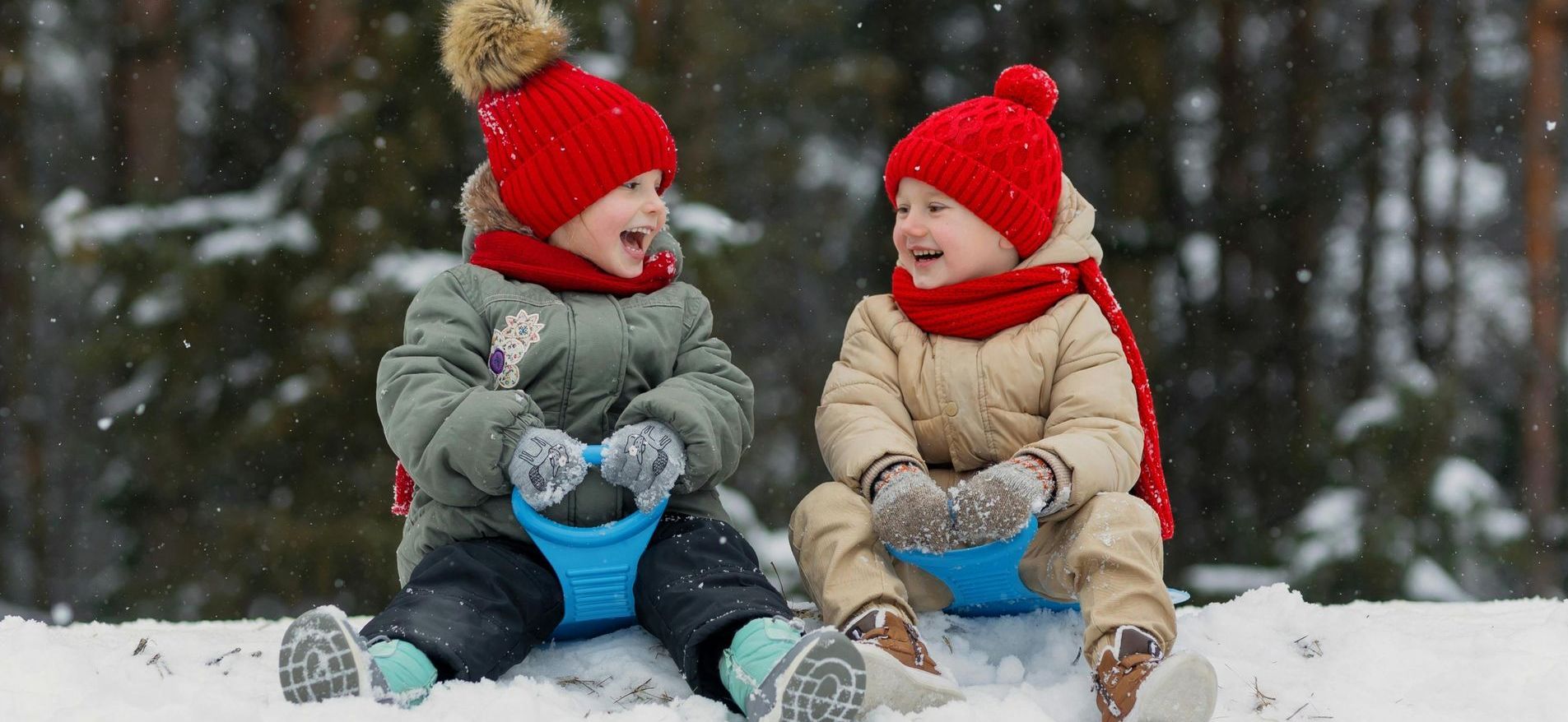 Two little boys are sitting on sleds in the snow.